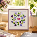 Decorative setup with a framed floral artwork, candles, and books on a wooden surface.