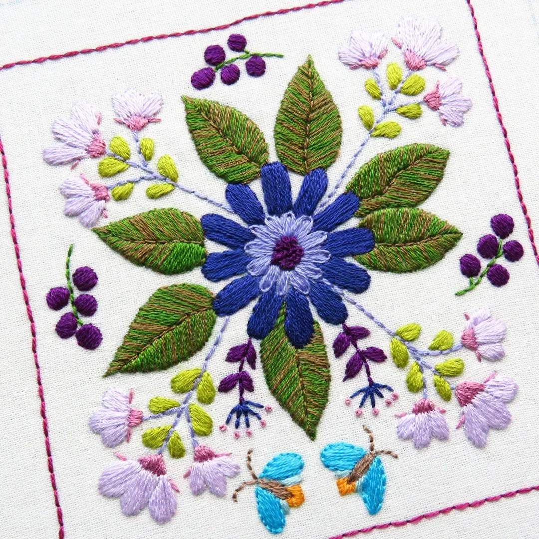 Embroidered floral design with blue flower and green leaves on a white background