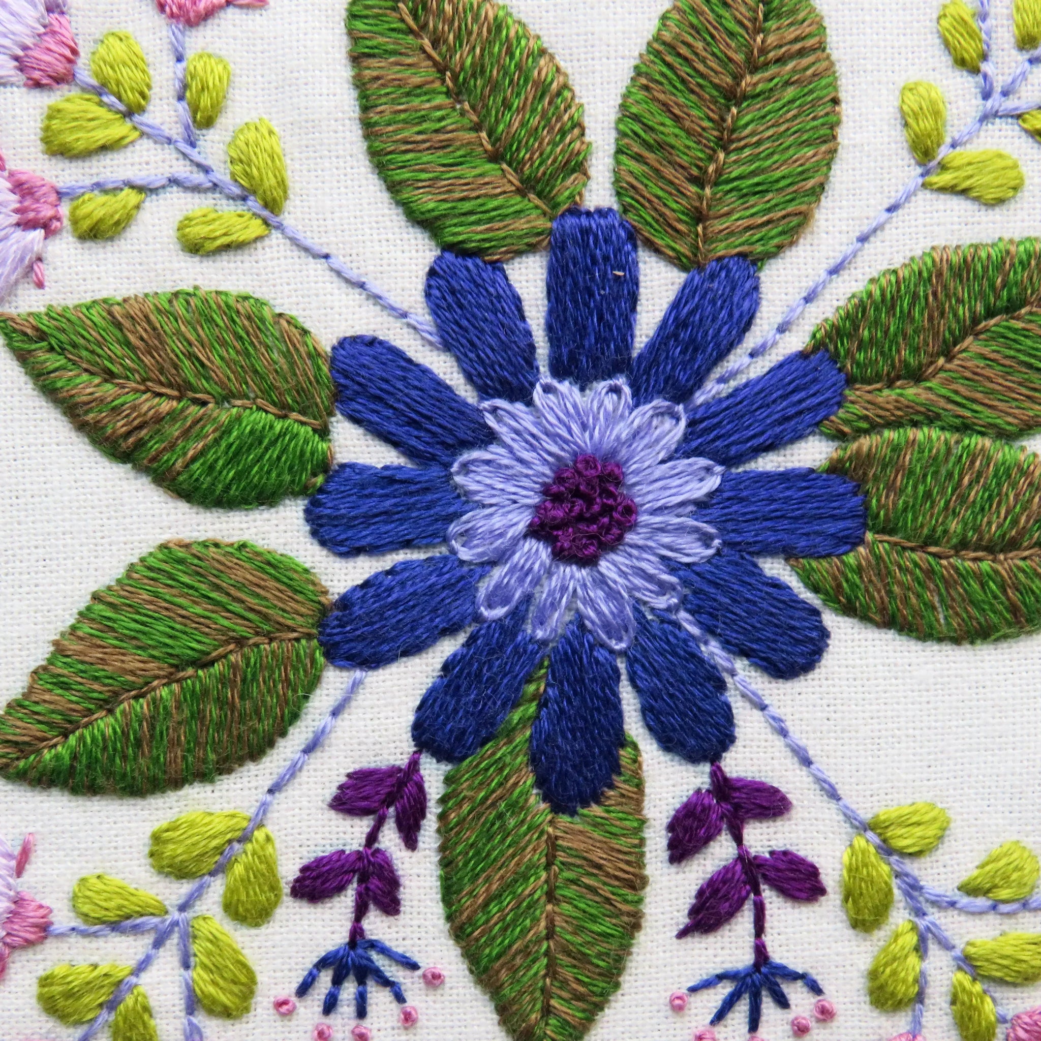 Close-up of embroidered floral design with blue flower and green leaves on white fabric.
