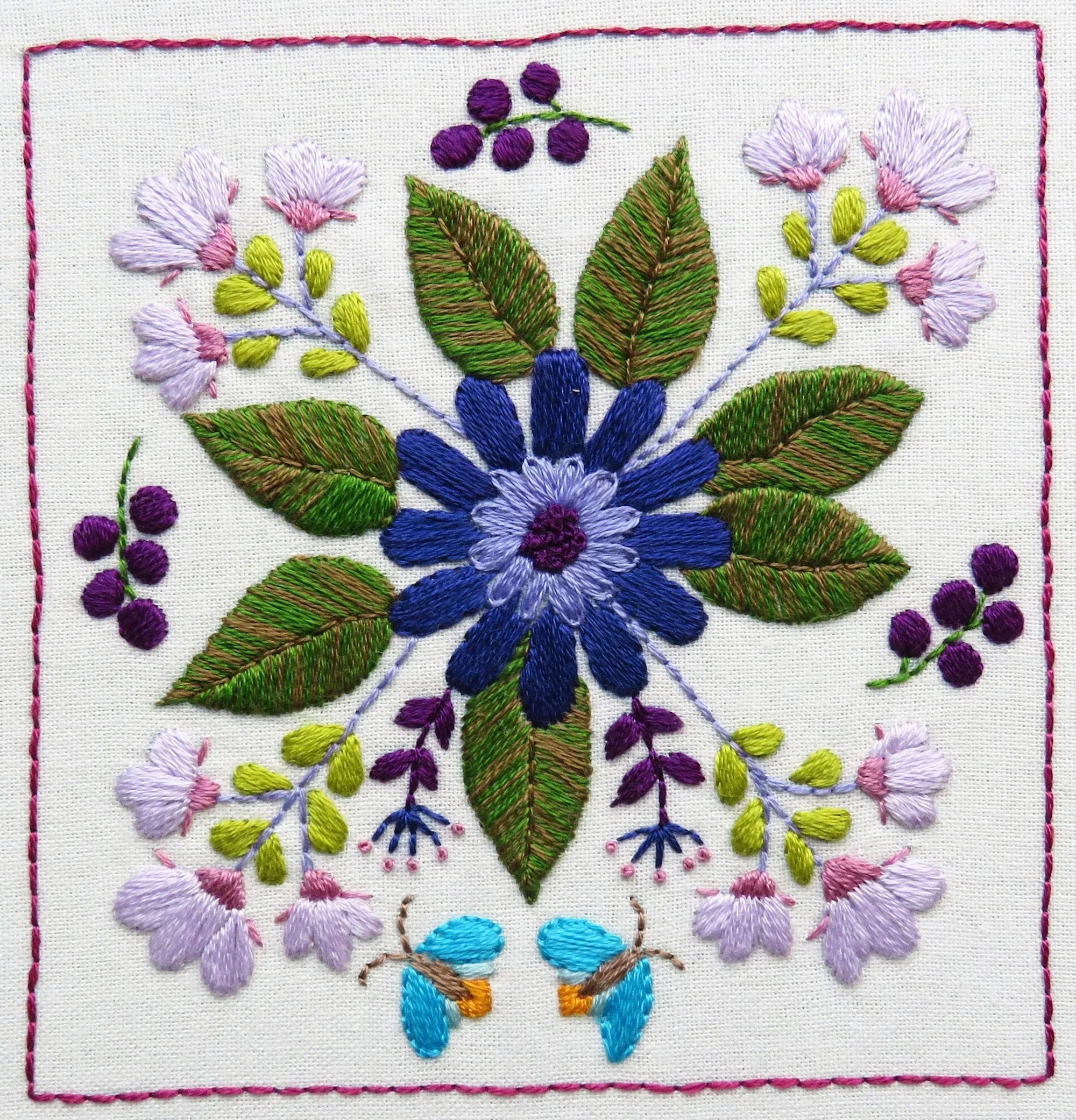 Embroidered design of a blue flower with green leaves and purple berries on a white background.