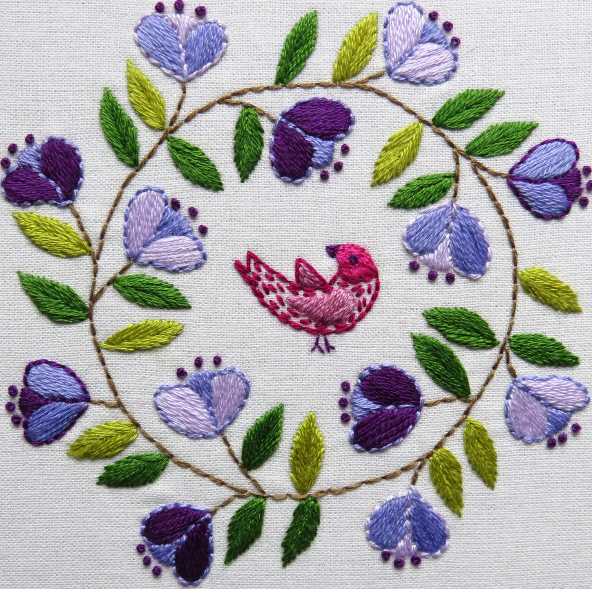Embroidery design with a bird surrounded by flowers and leaves.