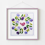 Embroidered artwork with a bird and floral design in a purple frame on a white background