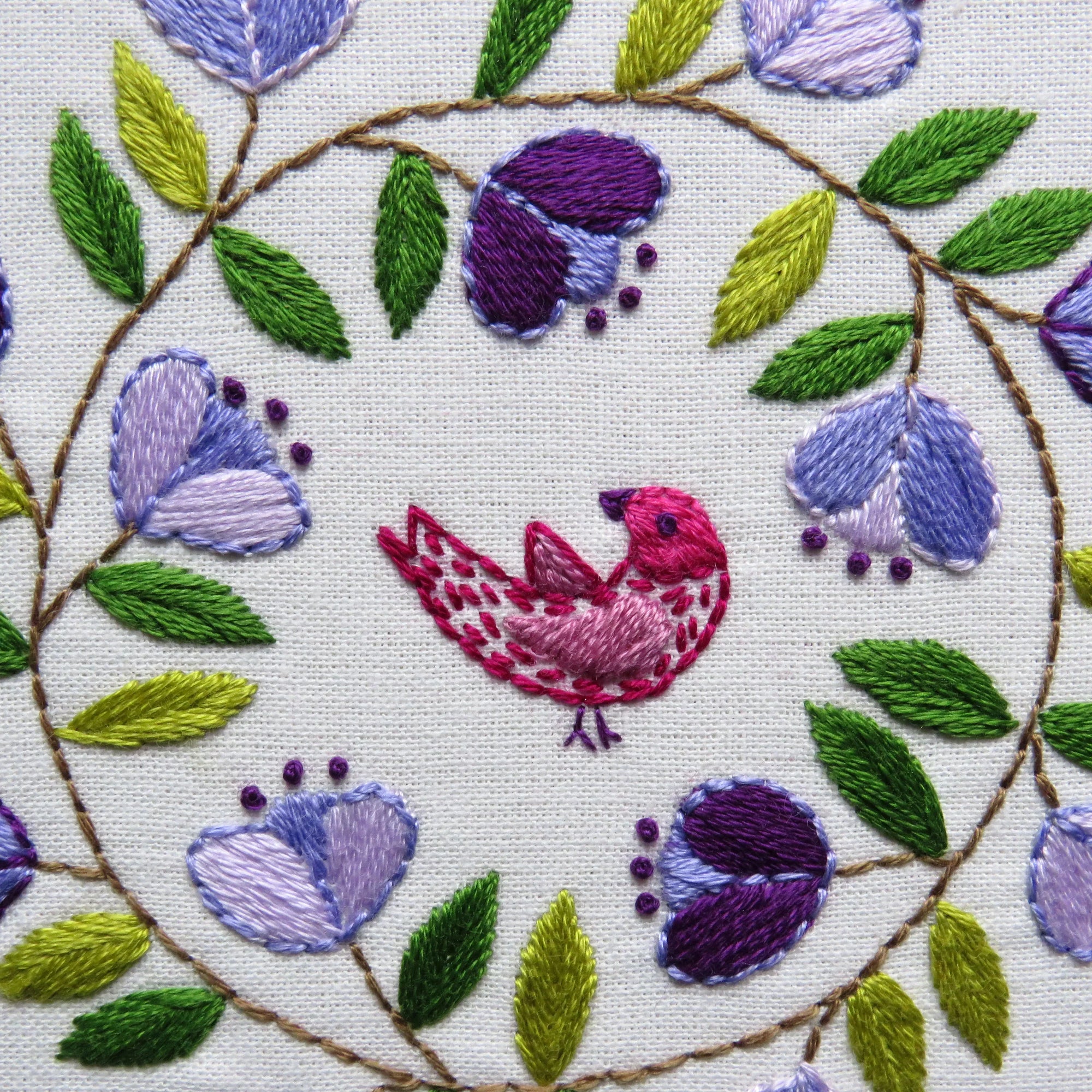 Embroidered design with a bird and floral patterns on white fabric.
