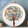 Embroidery hoop with a colorful tree design on fabric, against a gray background.