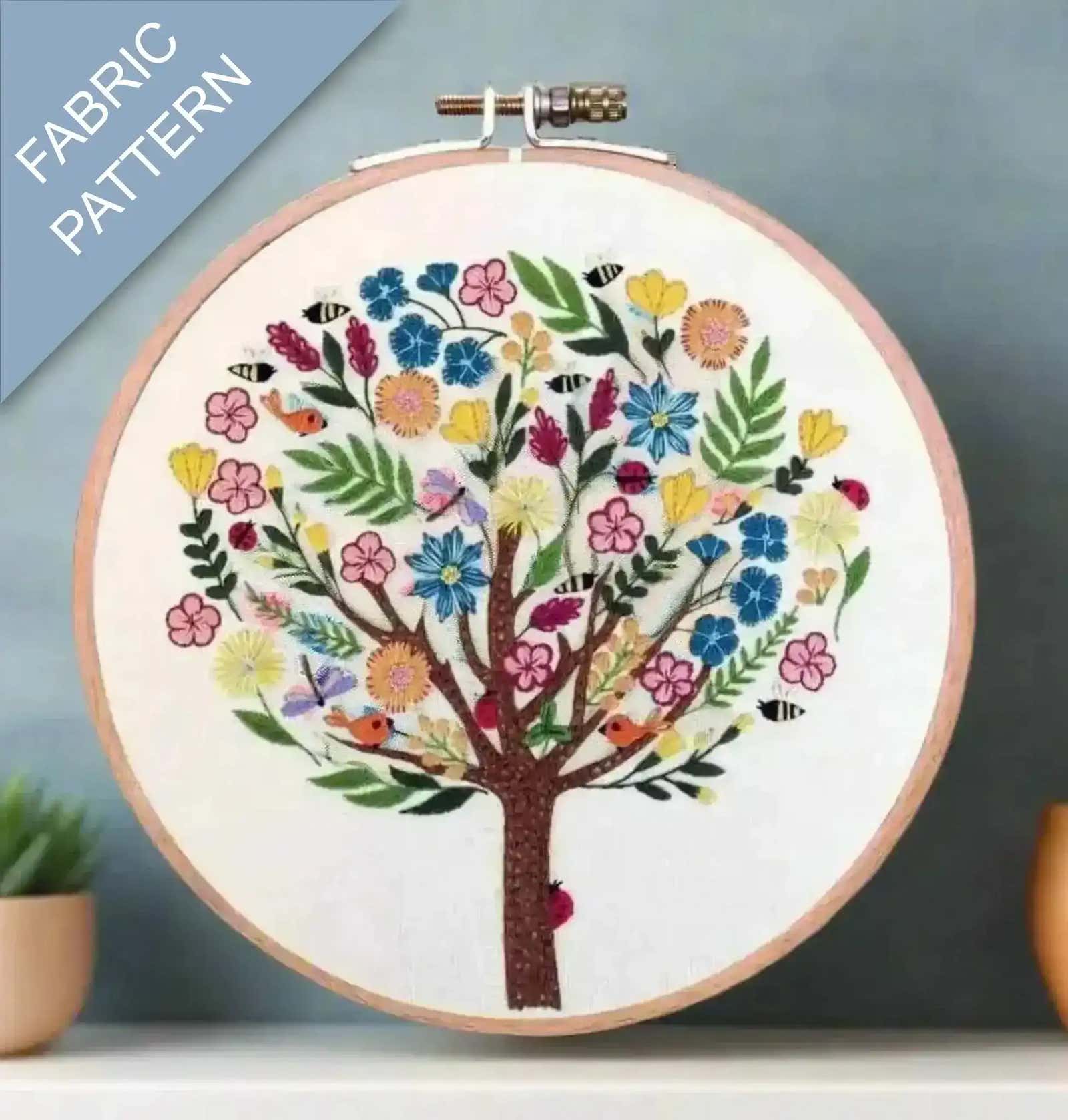 Embroidery hoop with a colorful tree design on fabric, against a gray background.