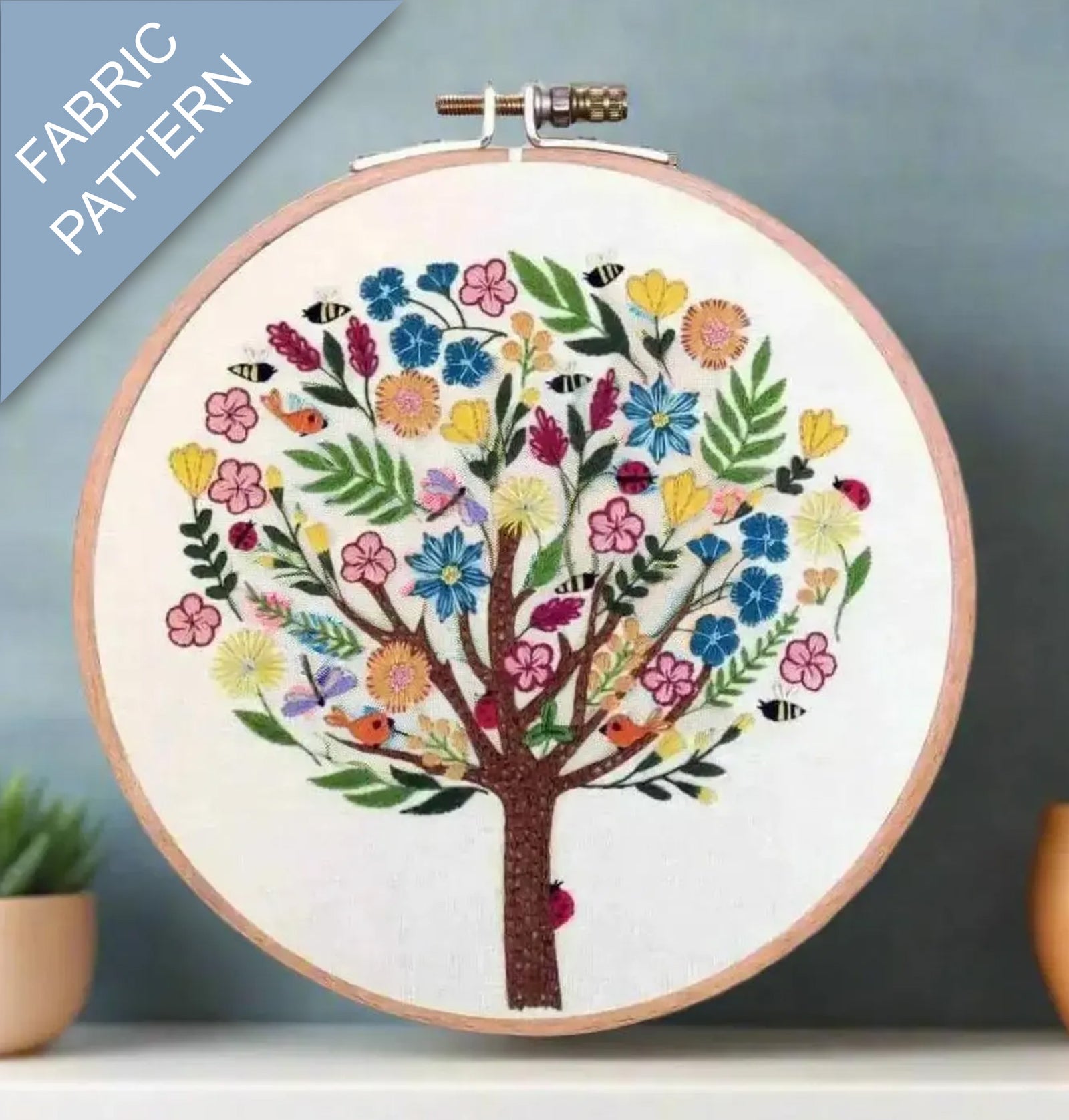 Embroidery hoop with a colorful tree design on fabric, against a gray background.
