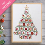Framed cross-stitch pattern in the shape of a Christmas tree on a wooden surface with decorative items.