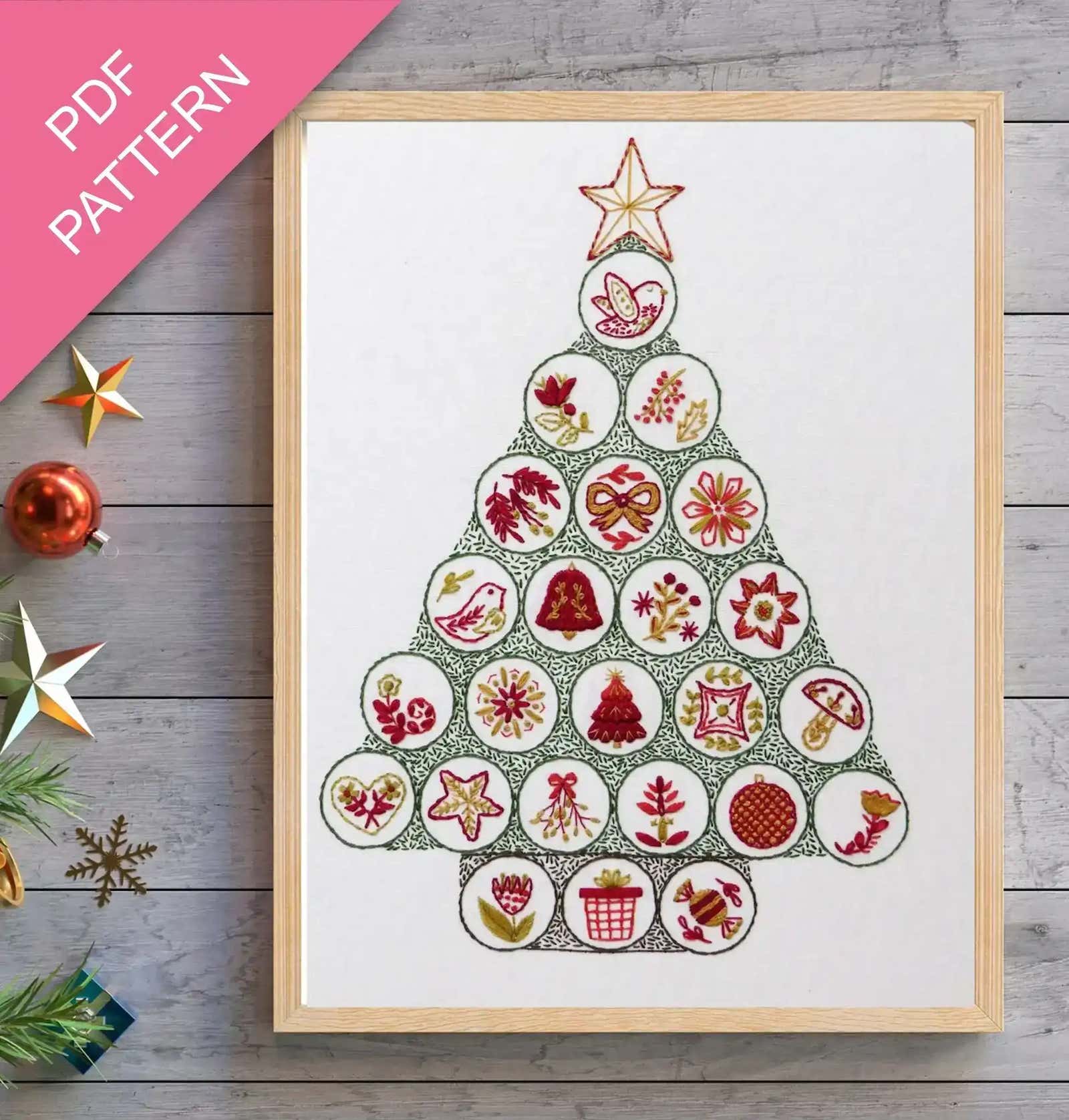 Framed cross-stitch pattern in the shape of a Christmas tree on a wooden surface with decorative items.