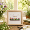 Framed artwork with floral design and text on a table with plants and scissors.