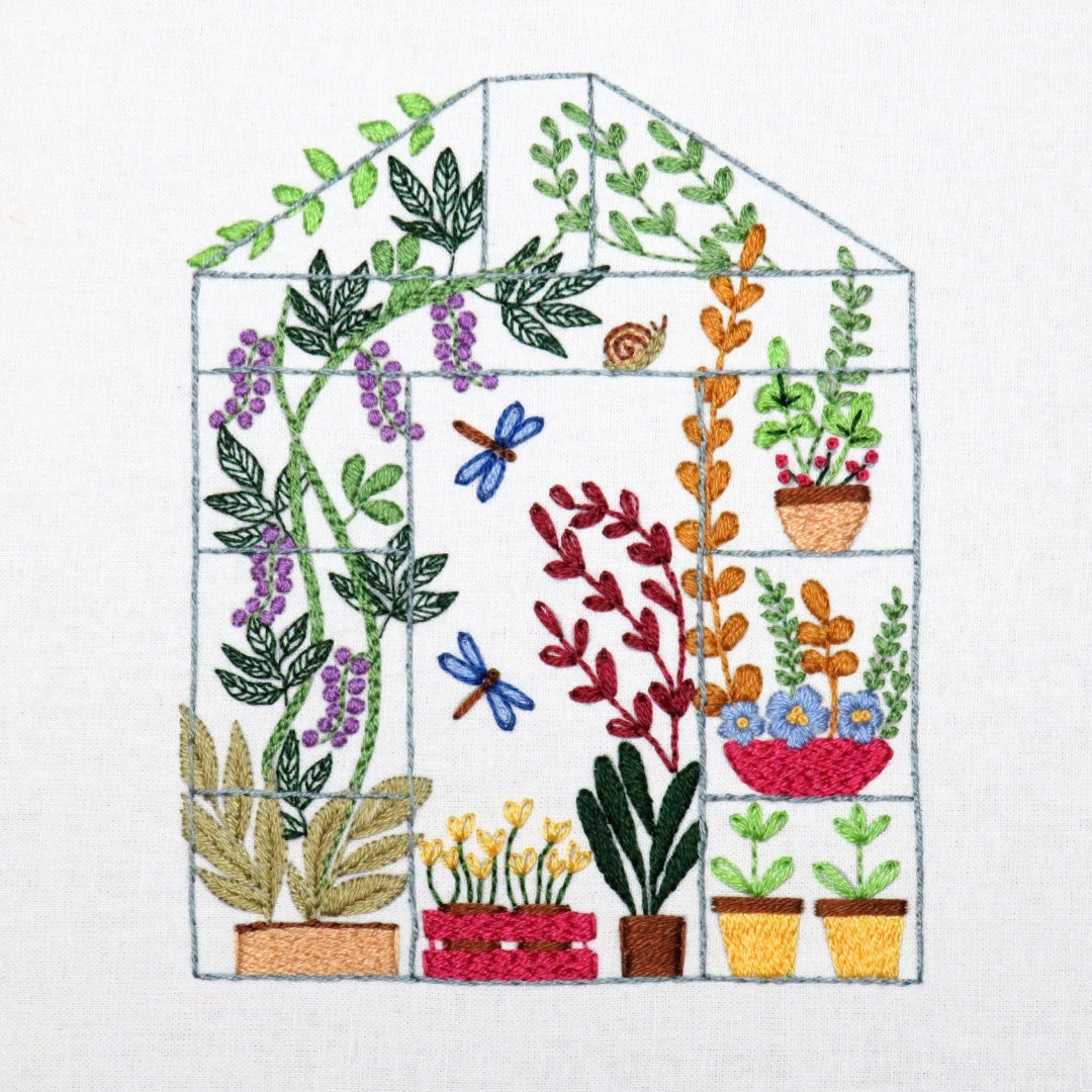 Embroidered design of a greenhouse with various plants and flowers on a white background