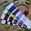 Color swatches with embroidery threads on a wooden surface with sewing tools.