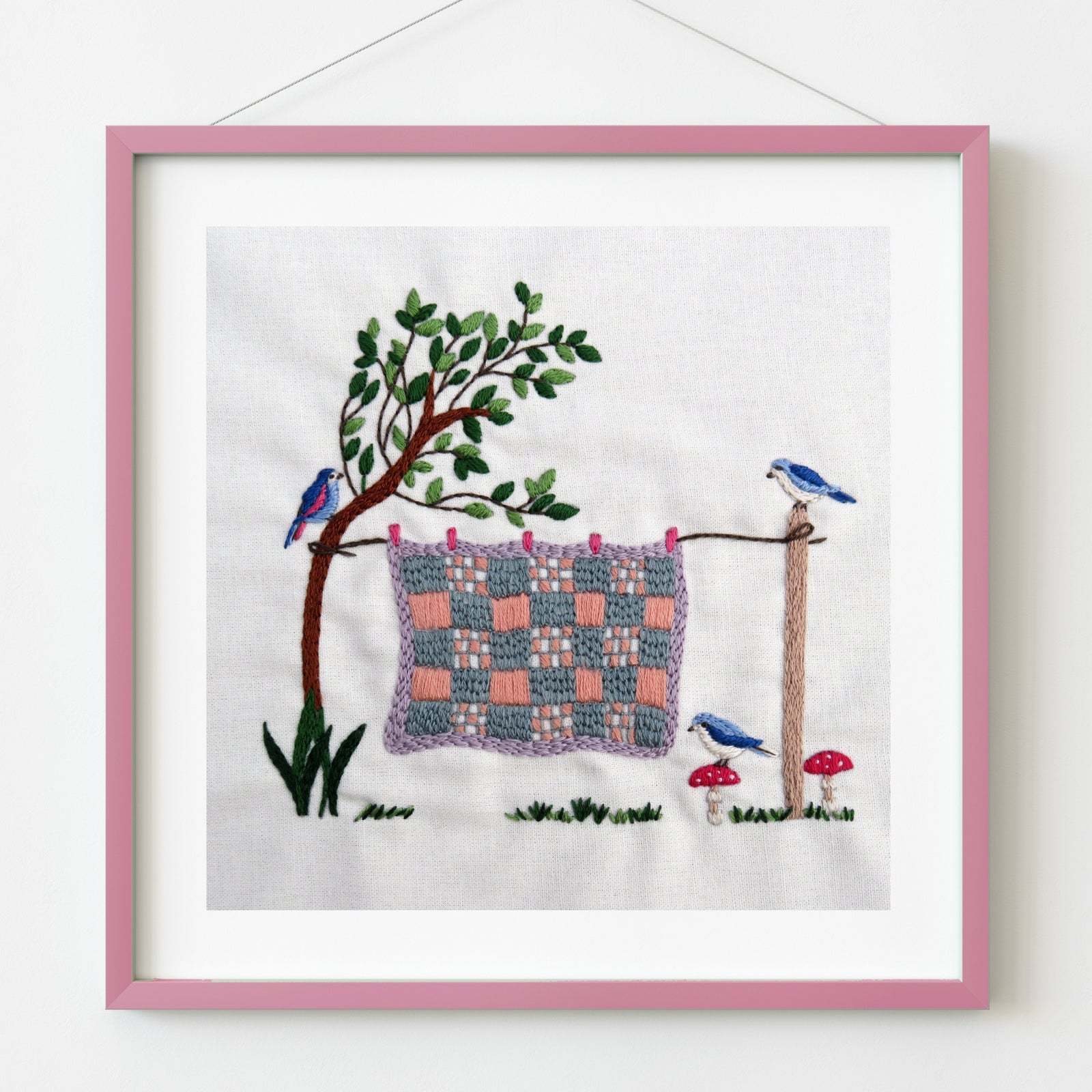 Embroidery of a tree with a woven pattern on fabric, surrounded by birds and plants, framed in pink.