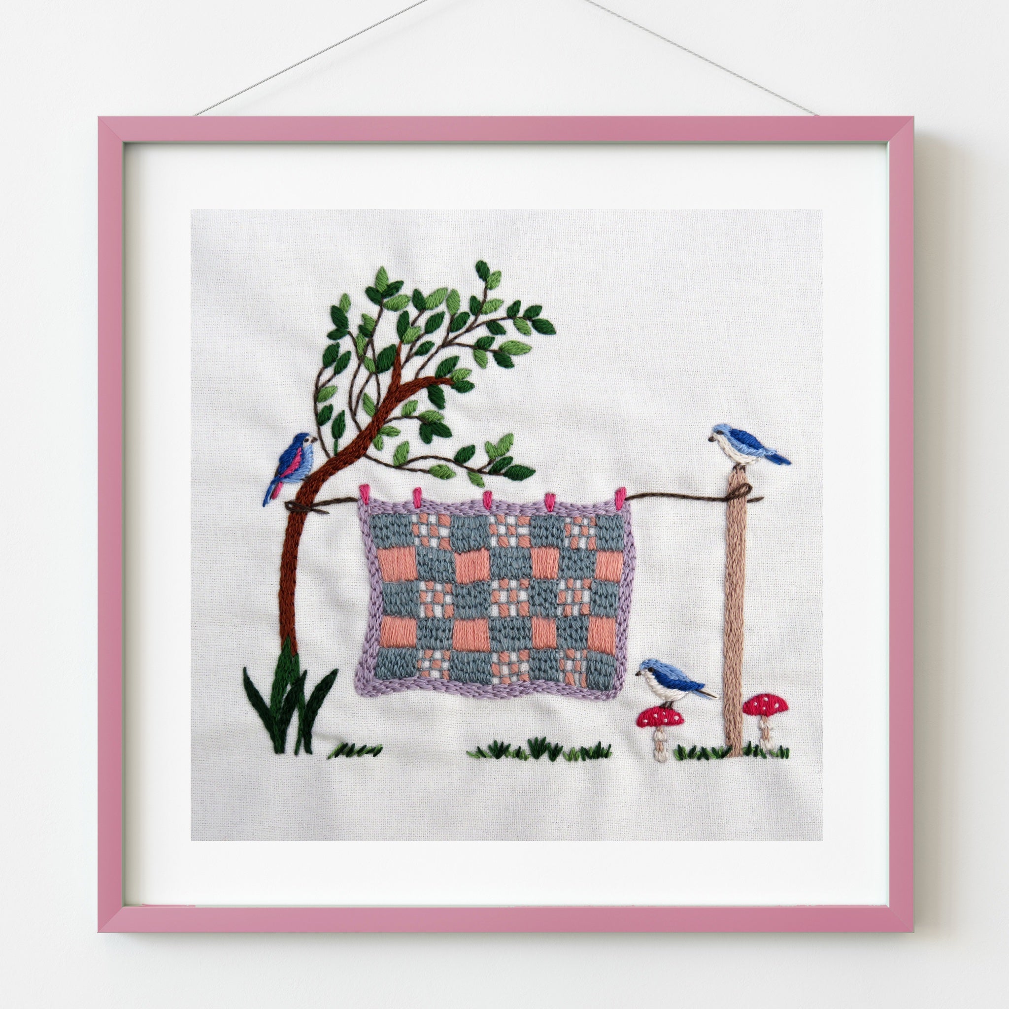 Embroidery of a tree with a woven pattern on fabric, surrounded by birds and plants, framed in pink.