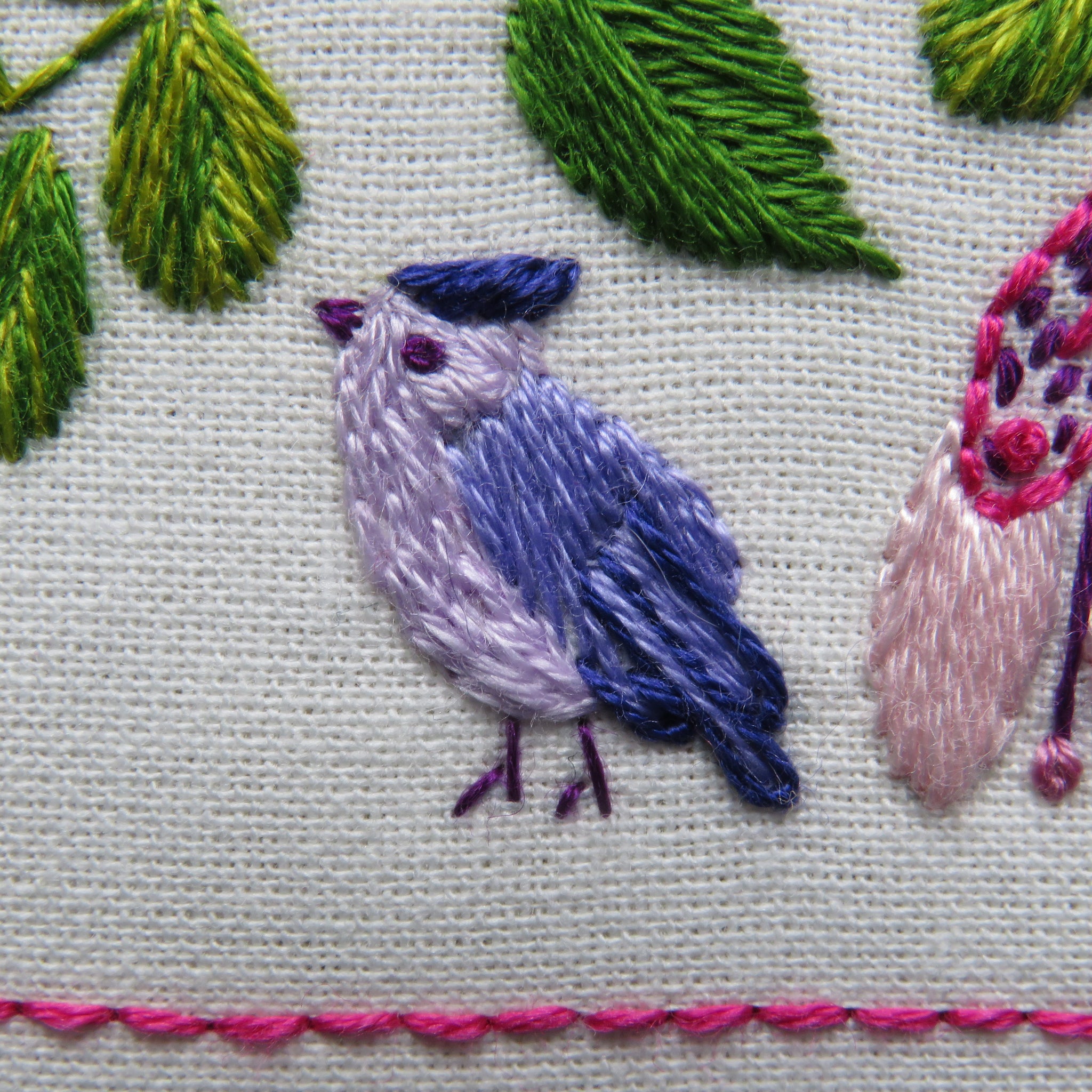 Embroidered design of a bird with green leaves and pink flowers on a light background