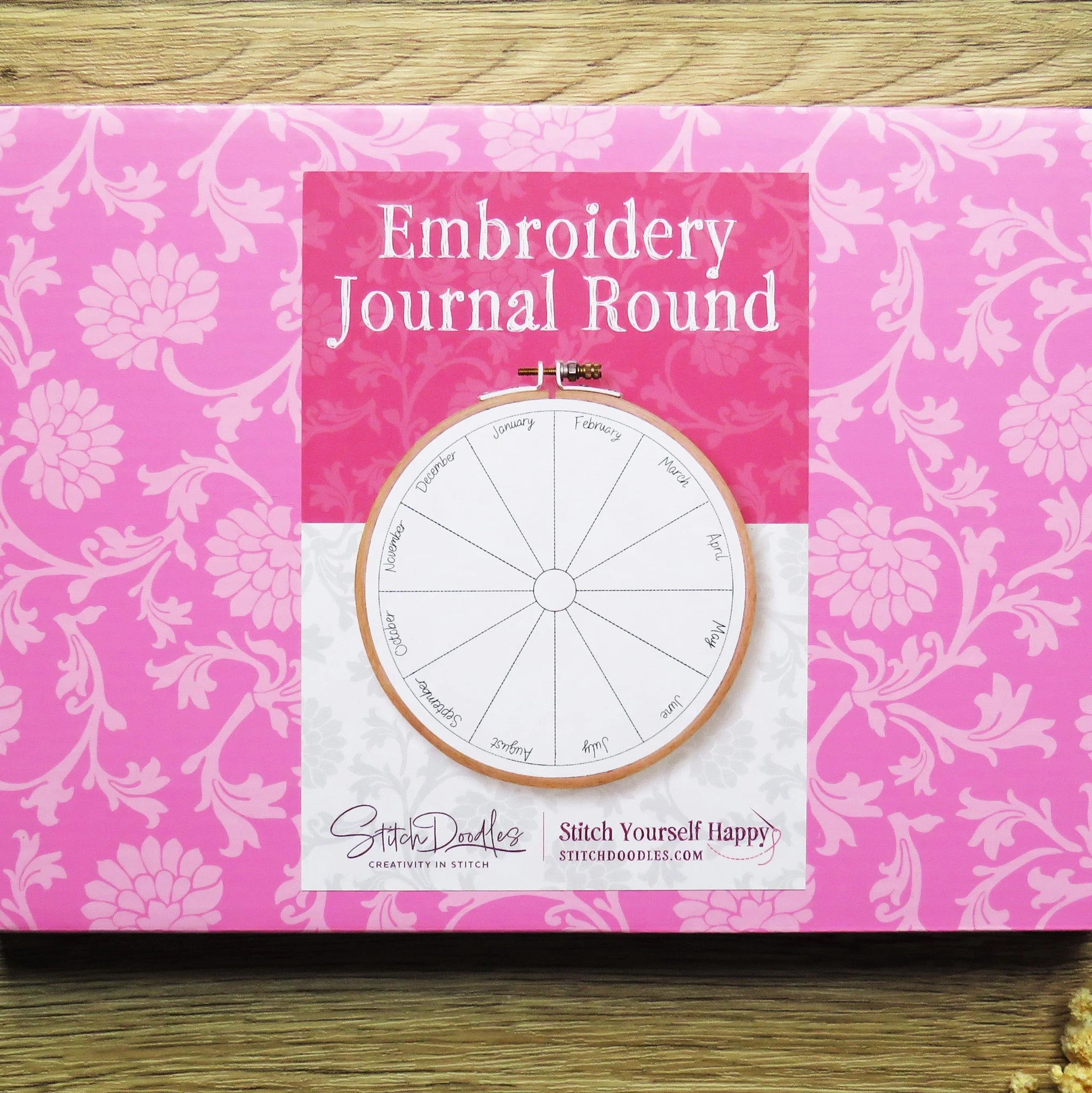 Pink embroidery journal with floral design on a wooden surface