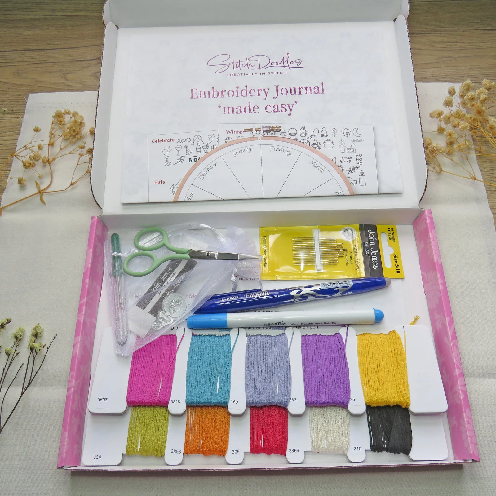 Embroidery kit with threads, scissors, and a book on a wooden surface.
