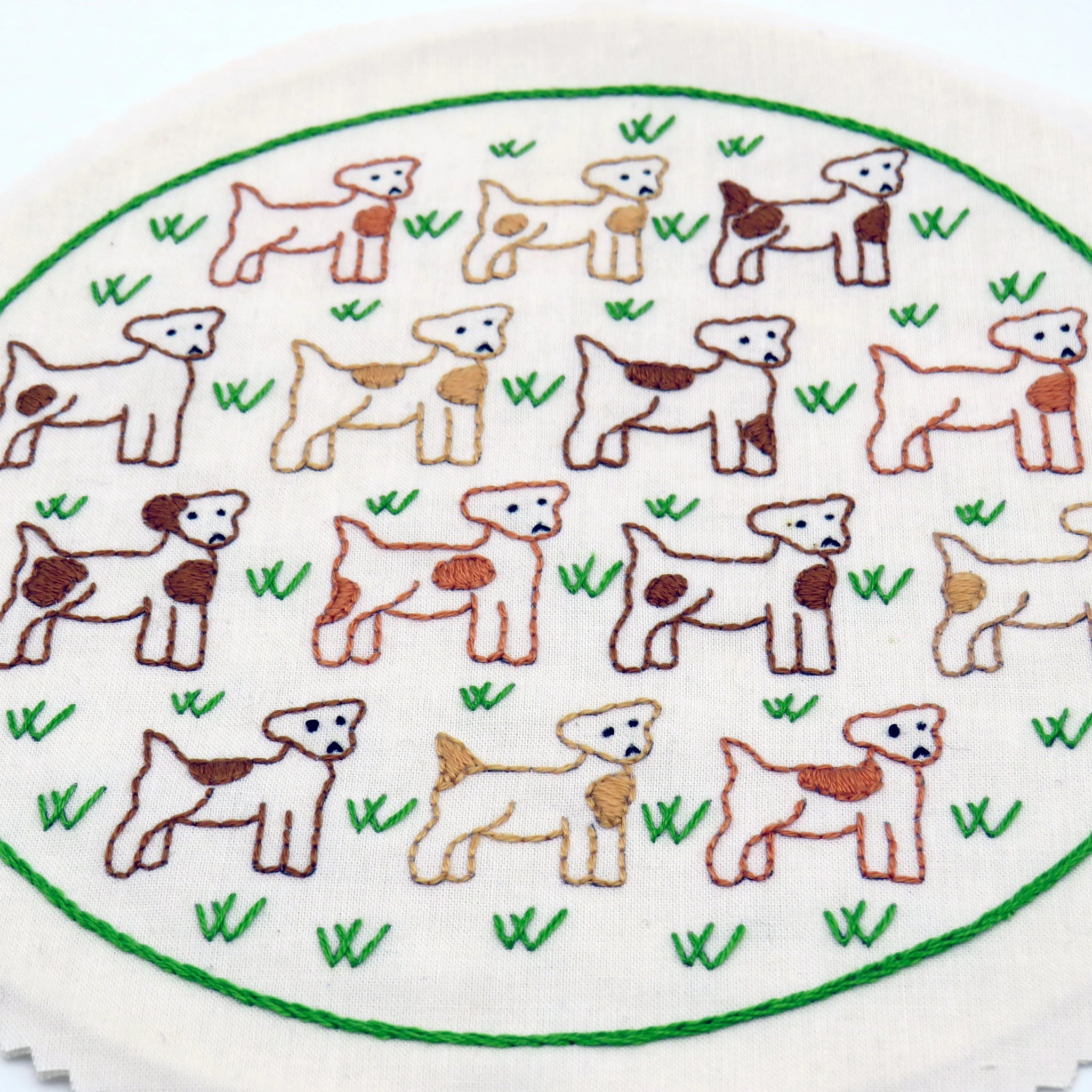 Embroidered pattern of dogs and puppies on a white background with green grass.