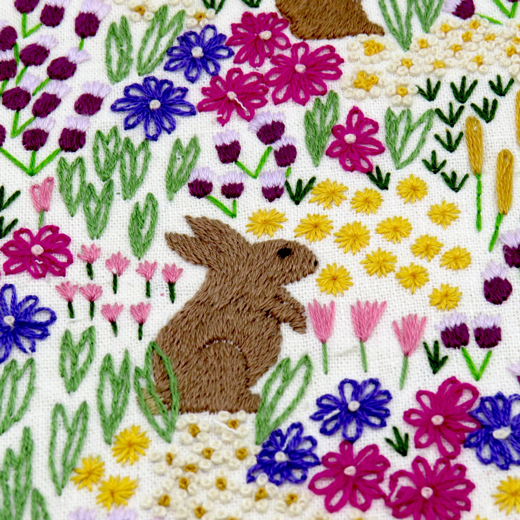 Embroidered design of a rabbit among colorful flowers on a white background