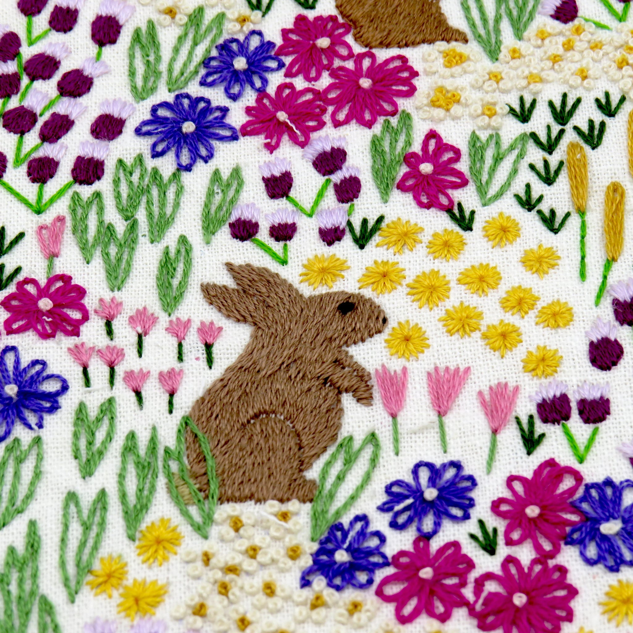 Embroidered design of a rabbit among colorful flowers on a white background
