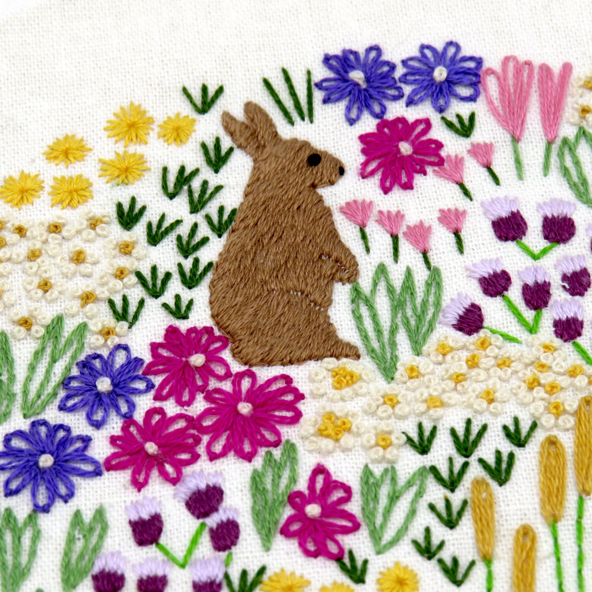 Embroidered design of a rabbit among flowers on a white background