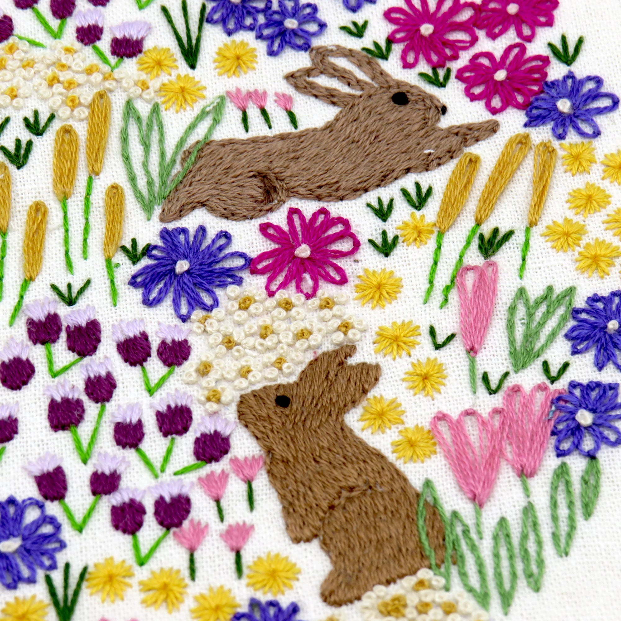 Embroidered design of two brown bunnies among colorful flowers