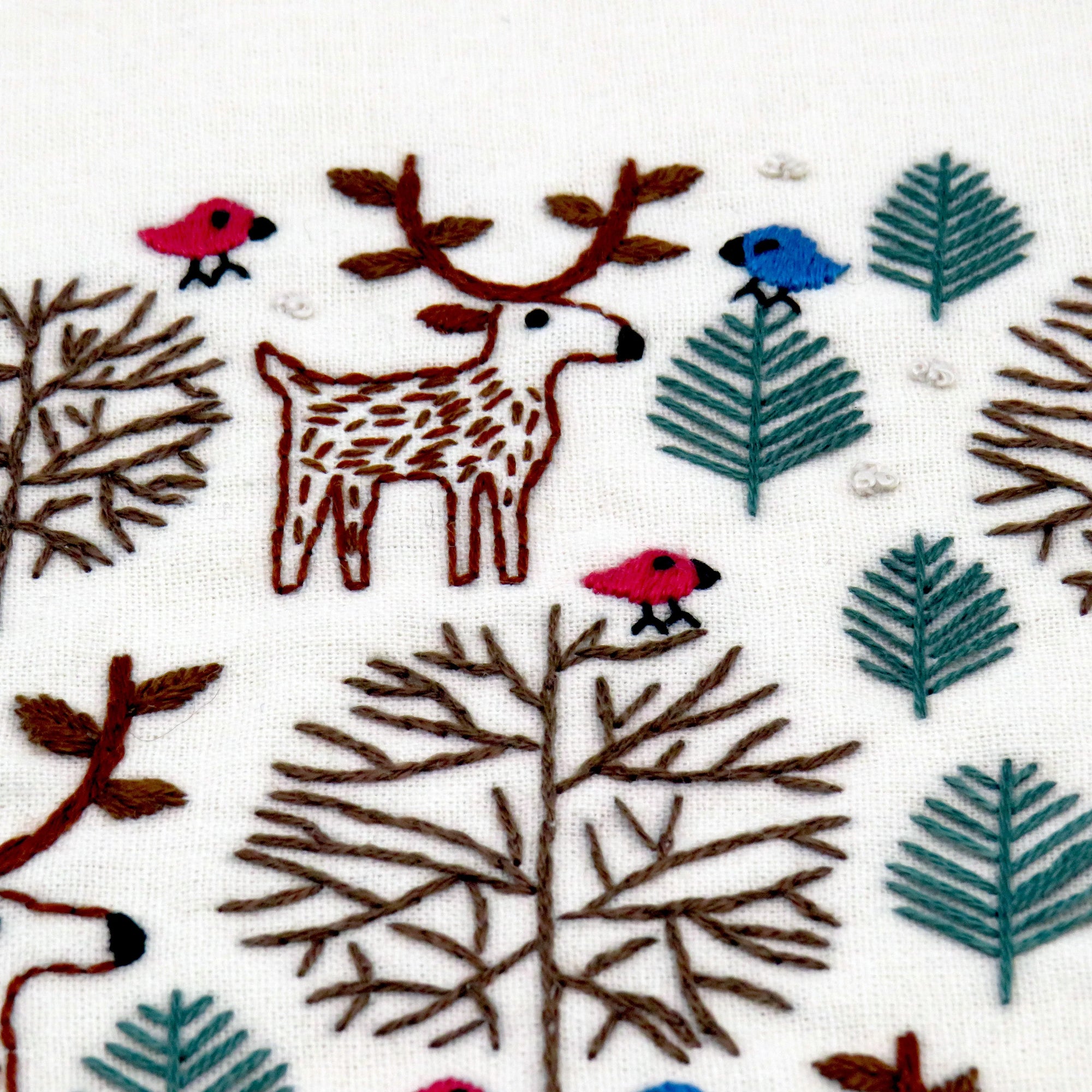 Embroidered design of a deer, birds, and trees on fabric.