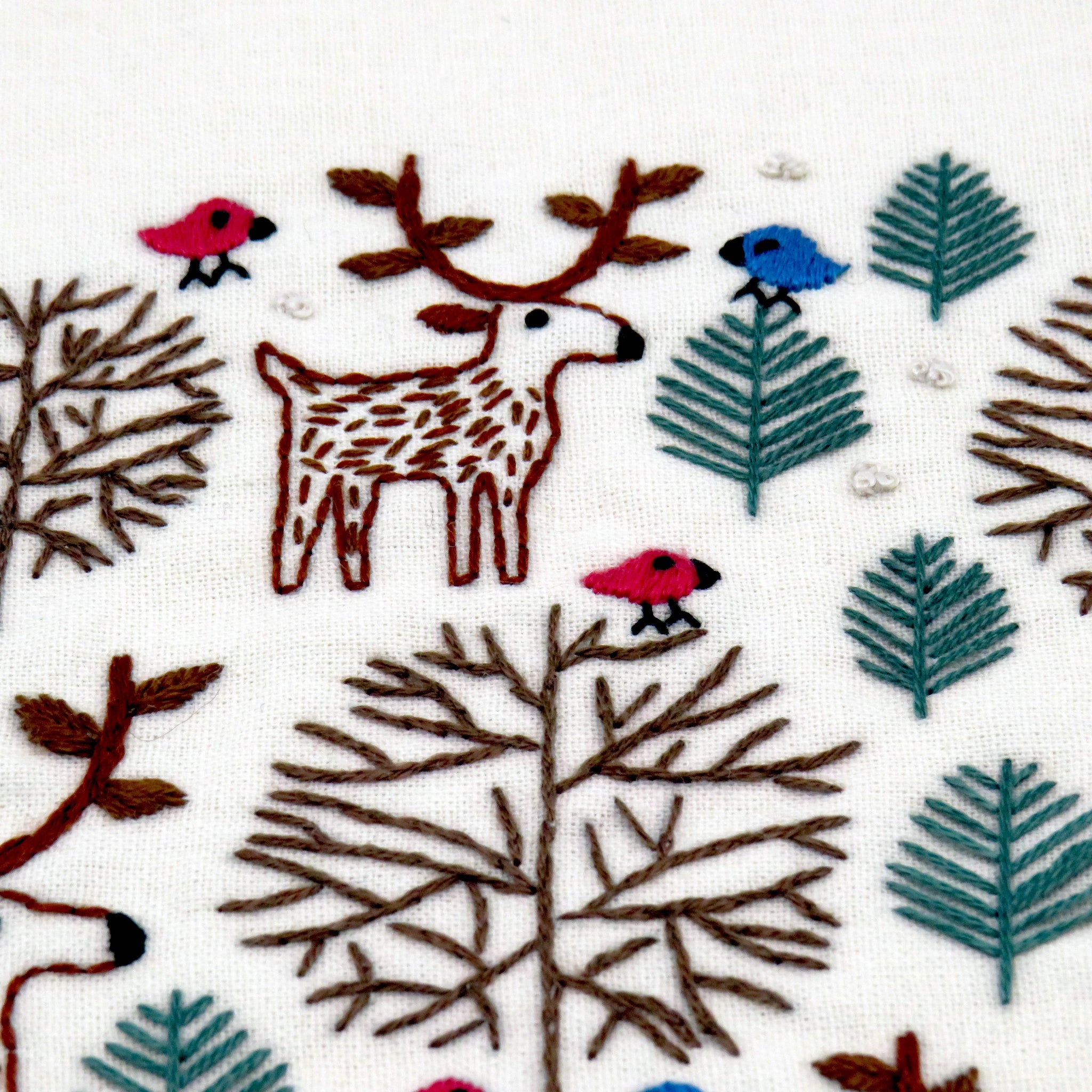 Embroidered design of a deer, birds, and trees on fabric.