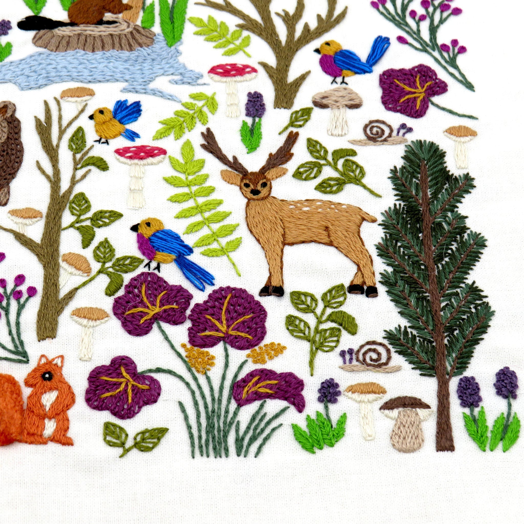 Collection of embroidered forest elements including trees, animals, and flowers on a white background.