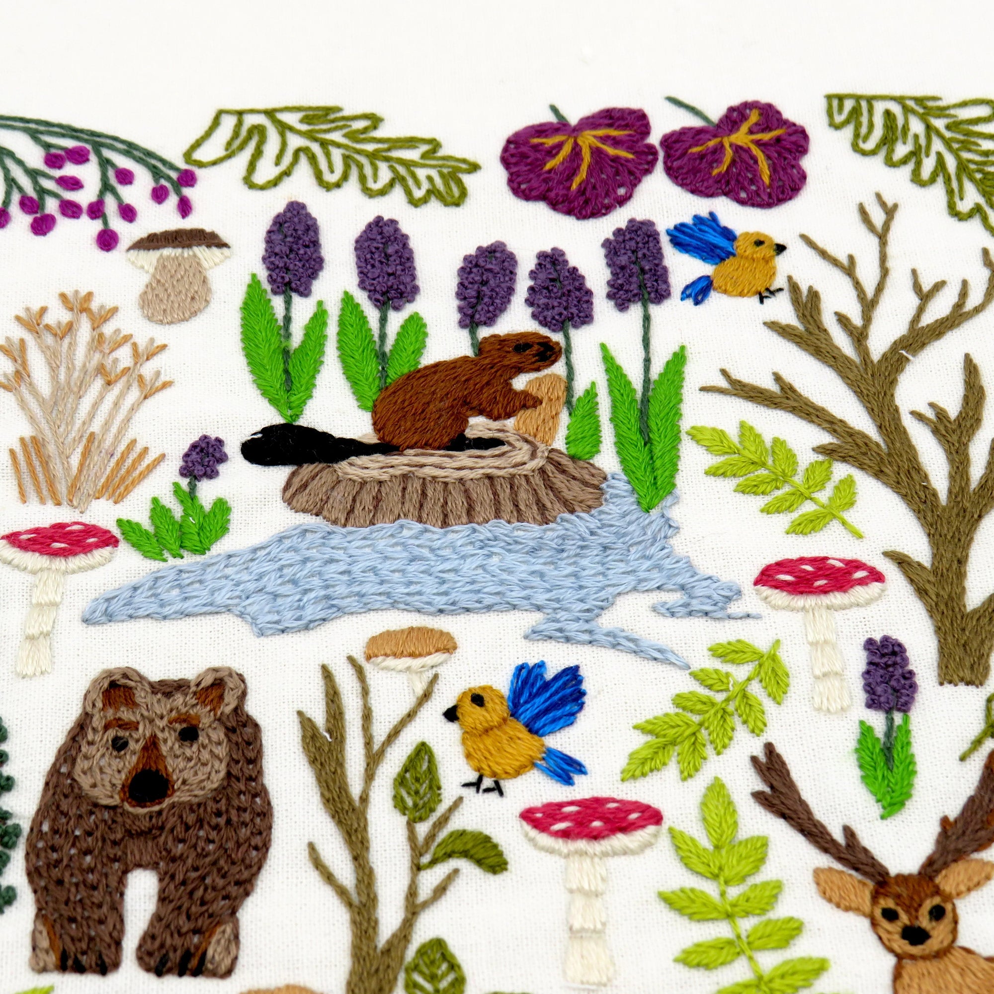 Embroidered design of a forest scene with animals, plants, and mushrooms.