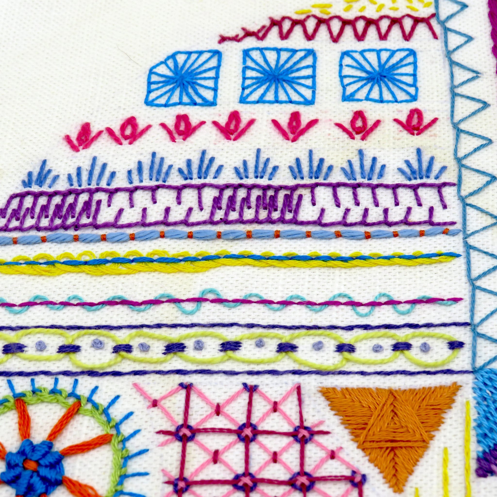 Colorful embroidered pattern with geometric shapes and floral elements on a white background