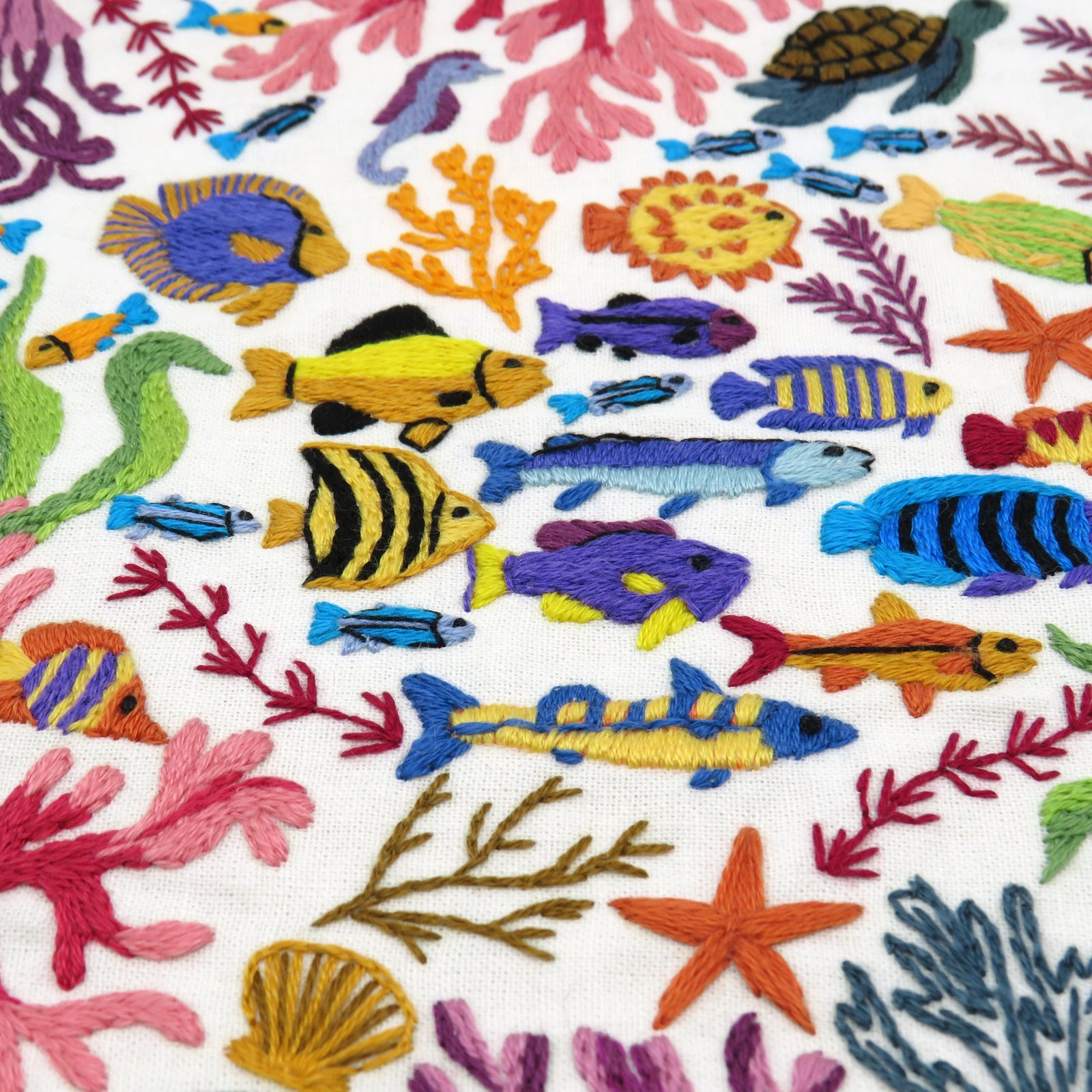 Colorful embroidered pattern of fish, coral, and sea stars on a white background