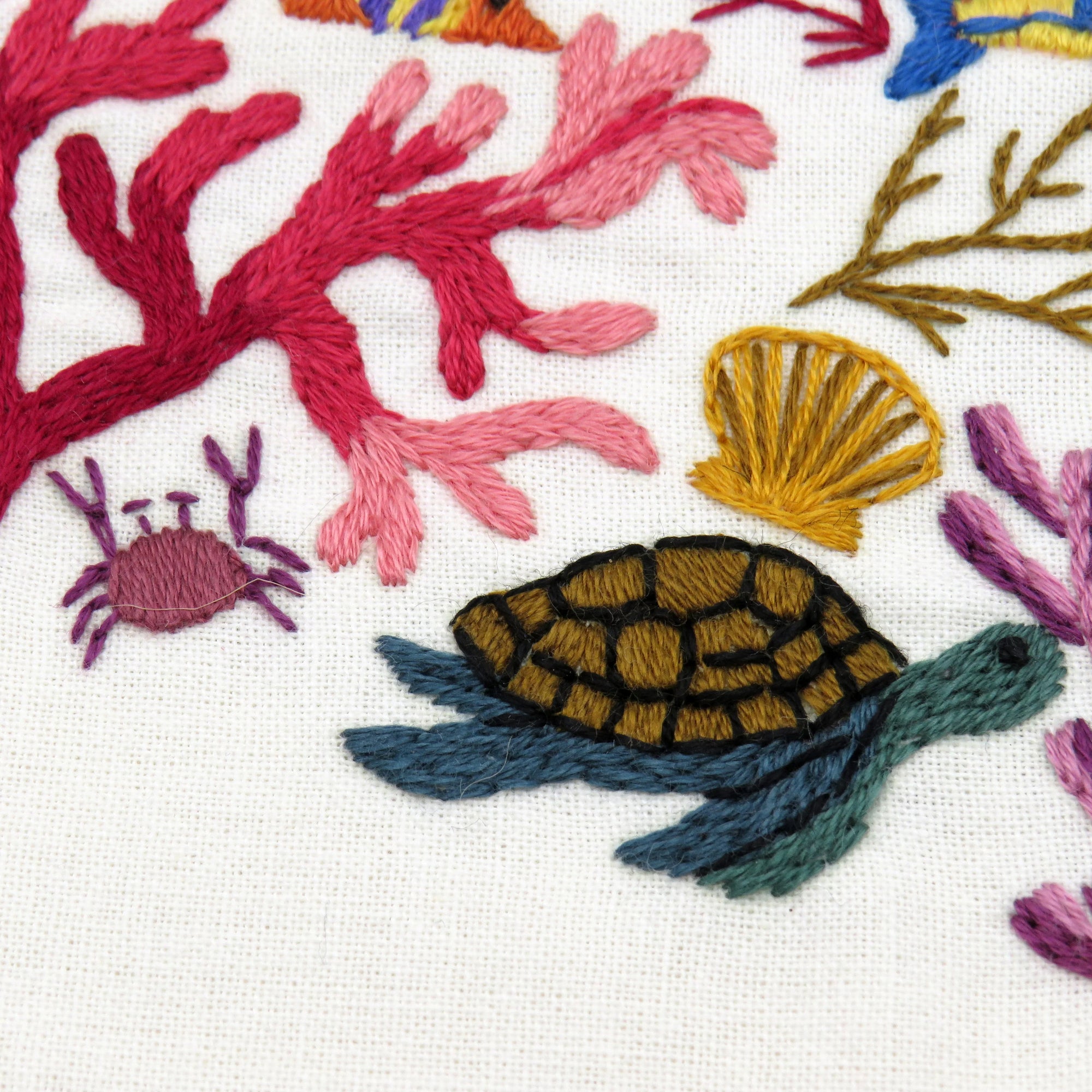Embroidered design of a turtle, shell, crab, and coral on fabric.