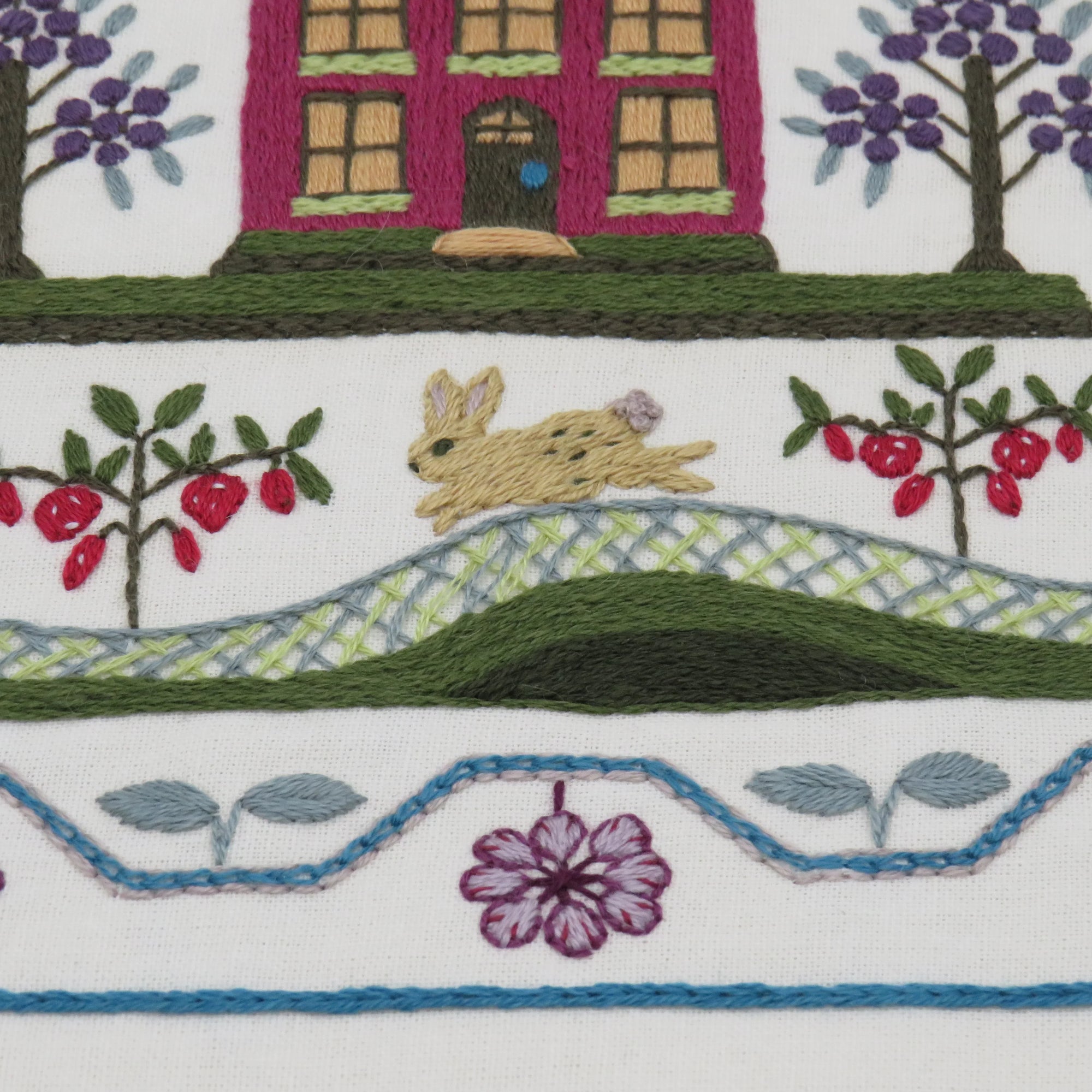 Embroidered scene with a house, rabbit, and nature elements on a white background