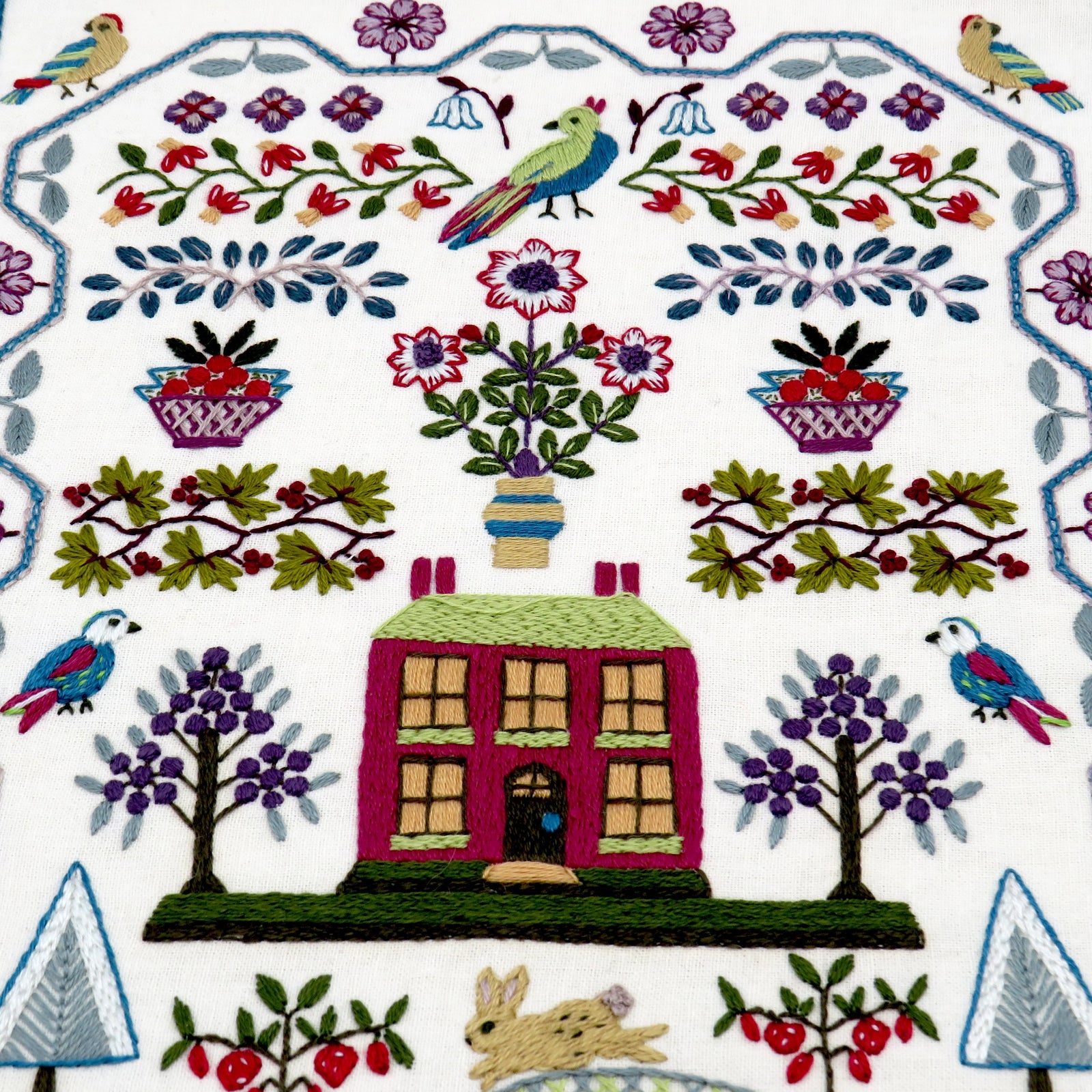 Embroidered design with a house, trees, flowers, and birds on a white background