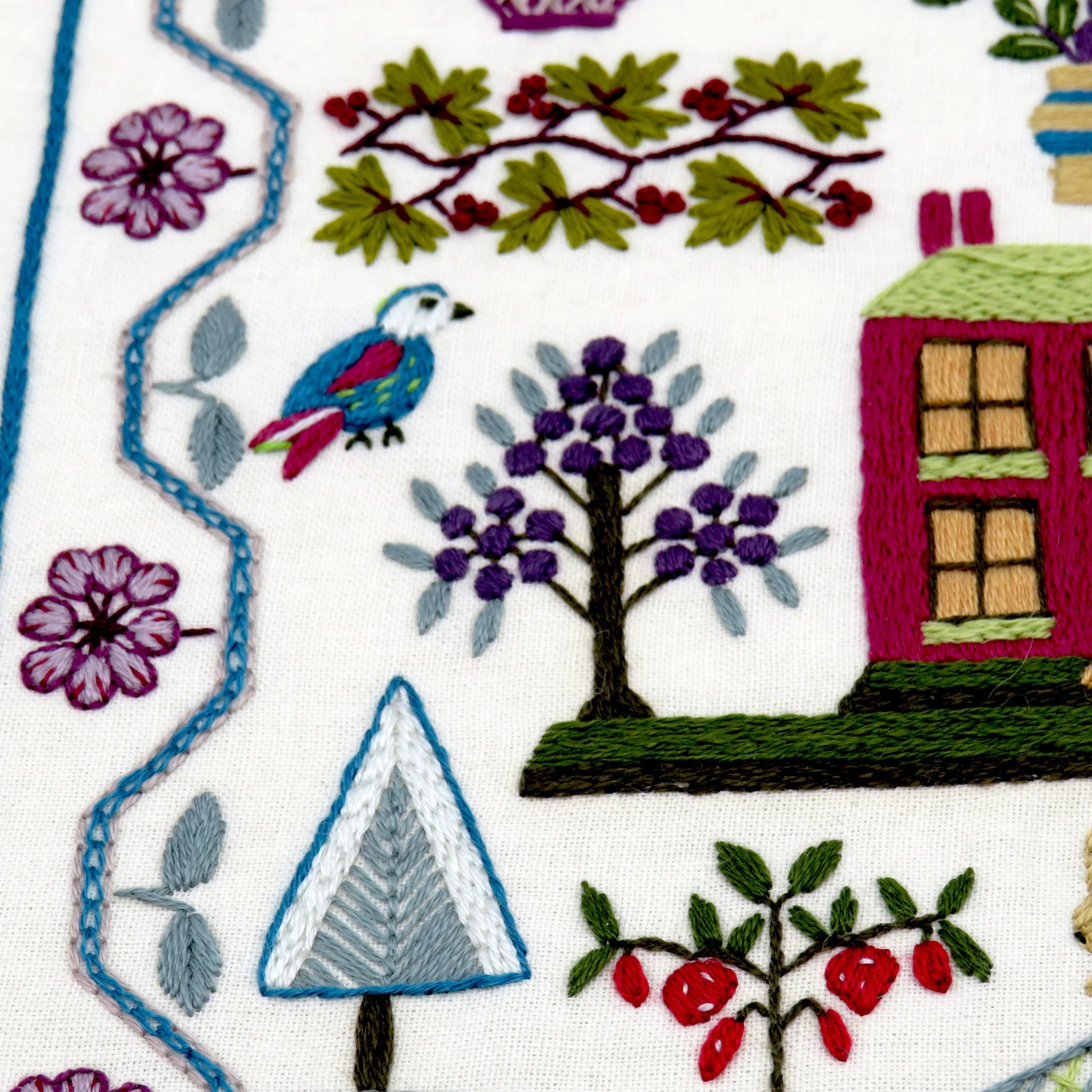 Embroidered design with houses, trees, and birds on a white background