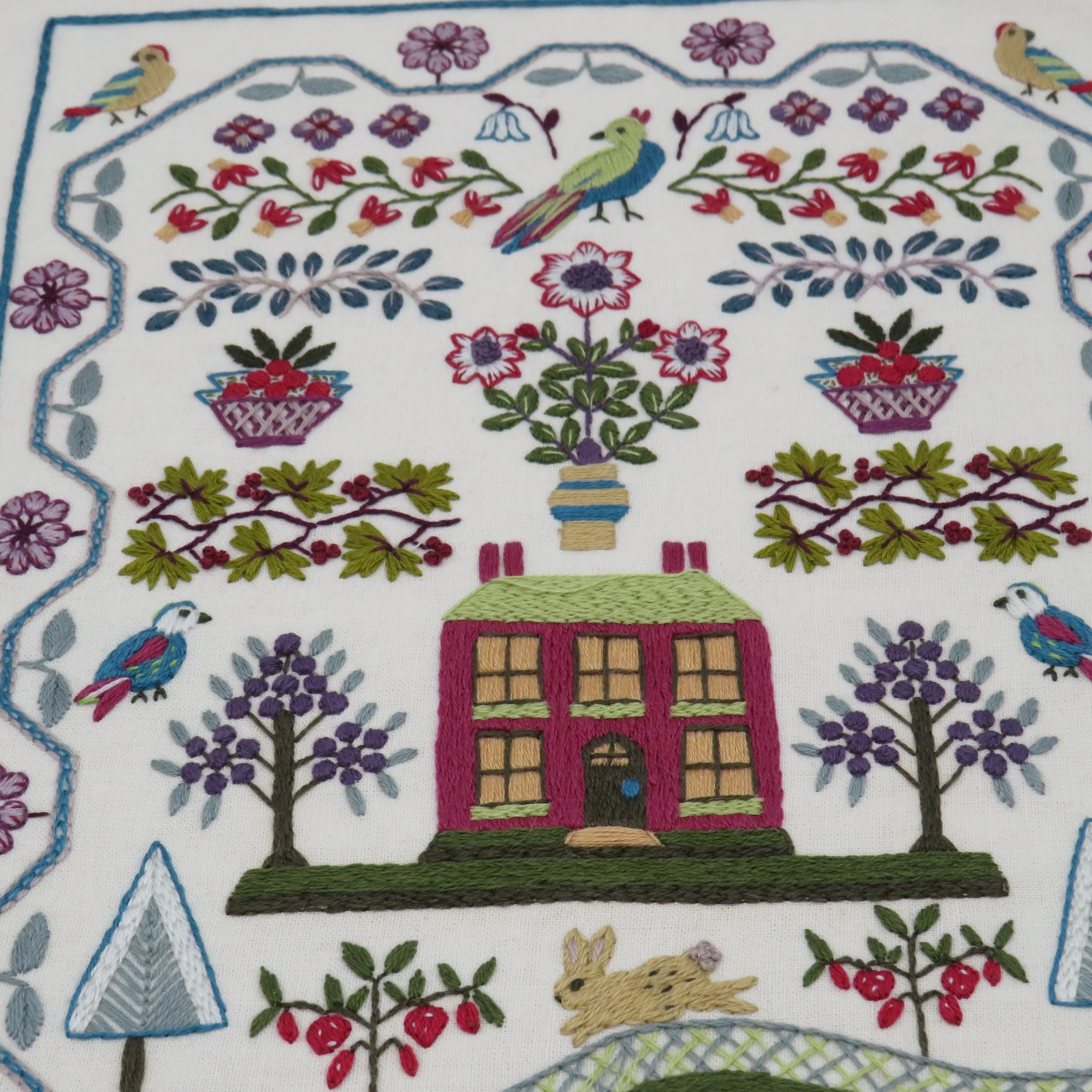 Embroidered design with a house, trees, and birds on a white background
