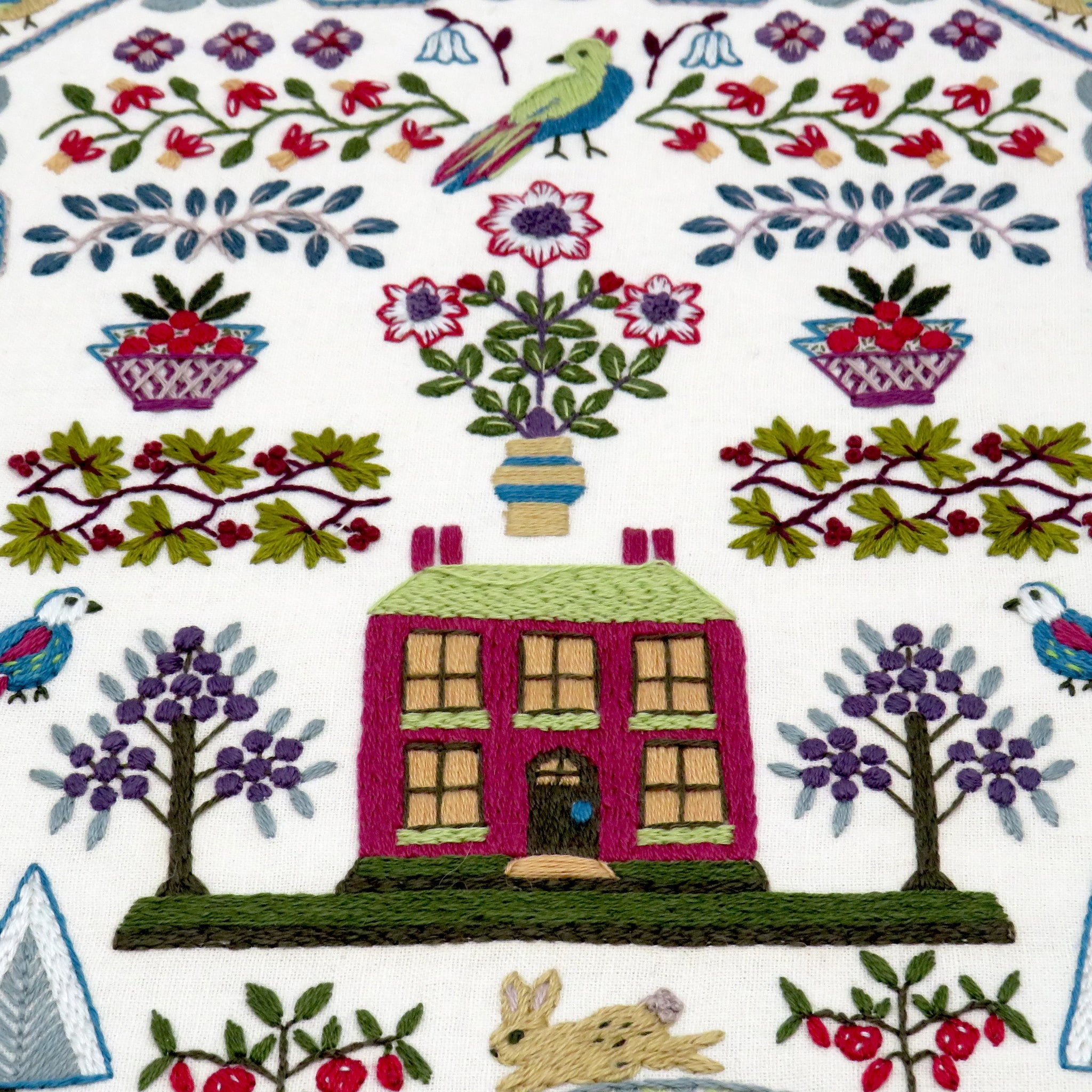 Embroidered fabric with a house, birds, and floral patterns on a white background