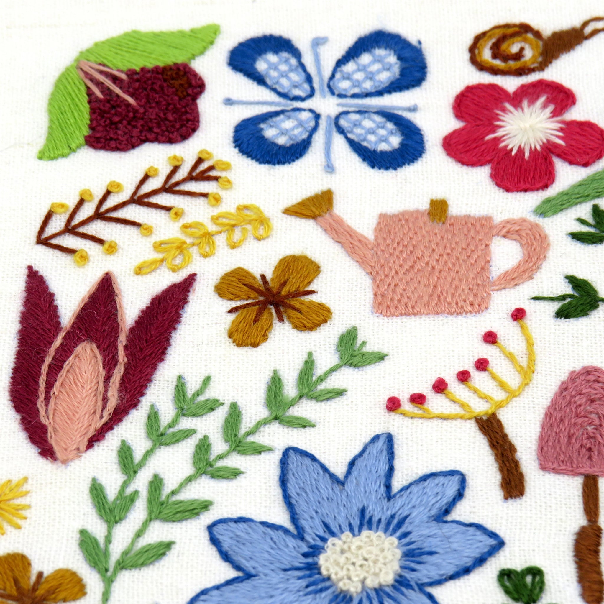 Embroidered design with flowers, leaves, and a watering can on a white background