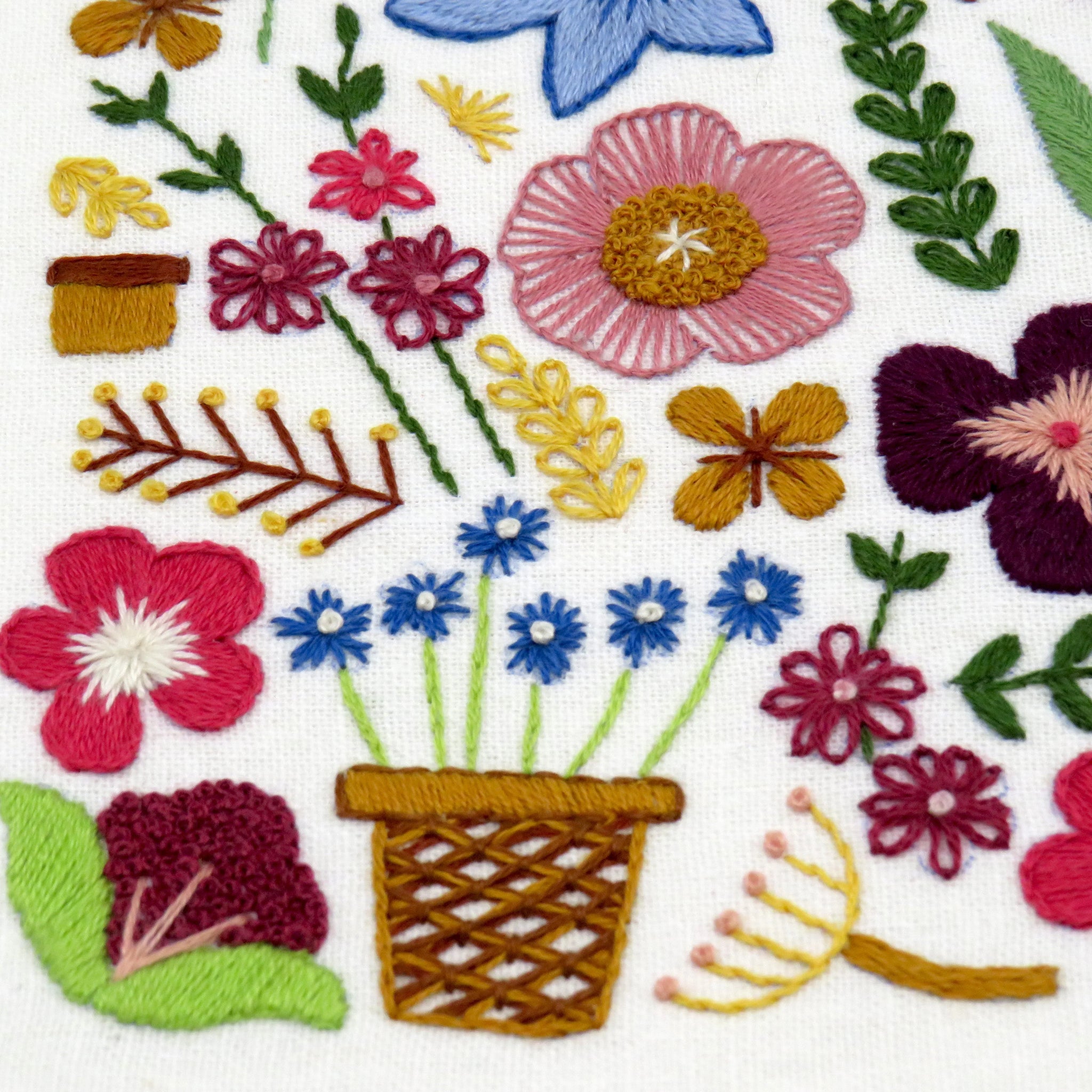 Embroidered design of flowers, plants, and a basket on a white background