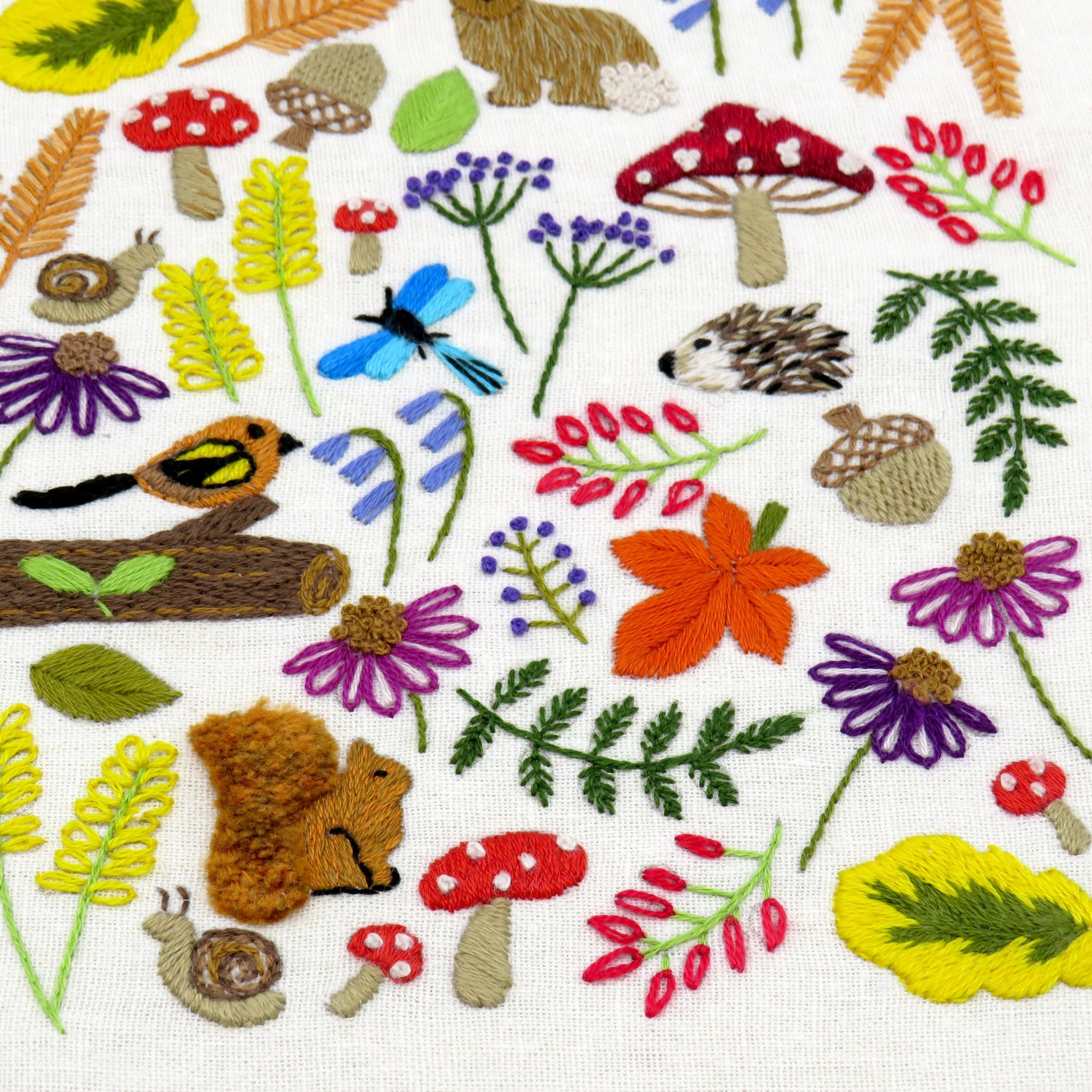Embroidered pattern with nature-themed elements including flowers, mushrooms, and animals on a white background.