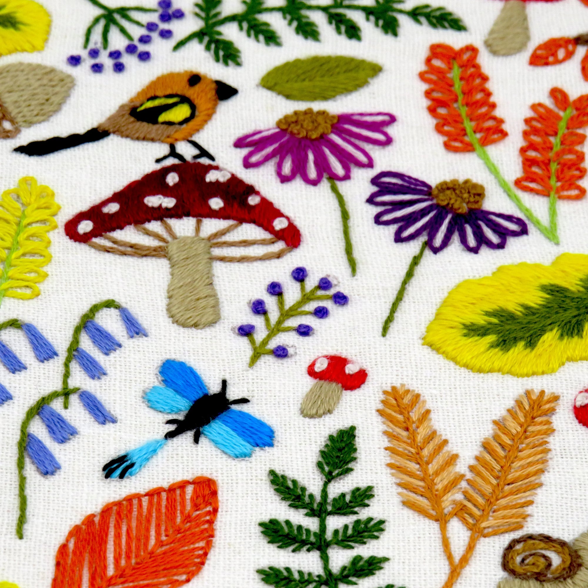 Embroidered fabric with colorful floral, butterfly, and mushroom designs on a white background