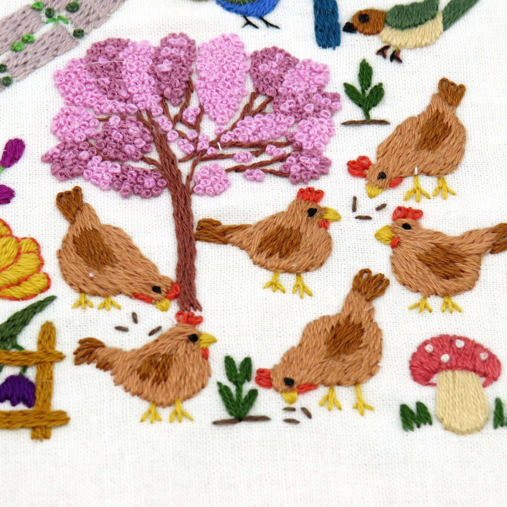 Embroidered design of chickens, trees, flowers, and mushrooms on fabric.