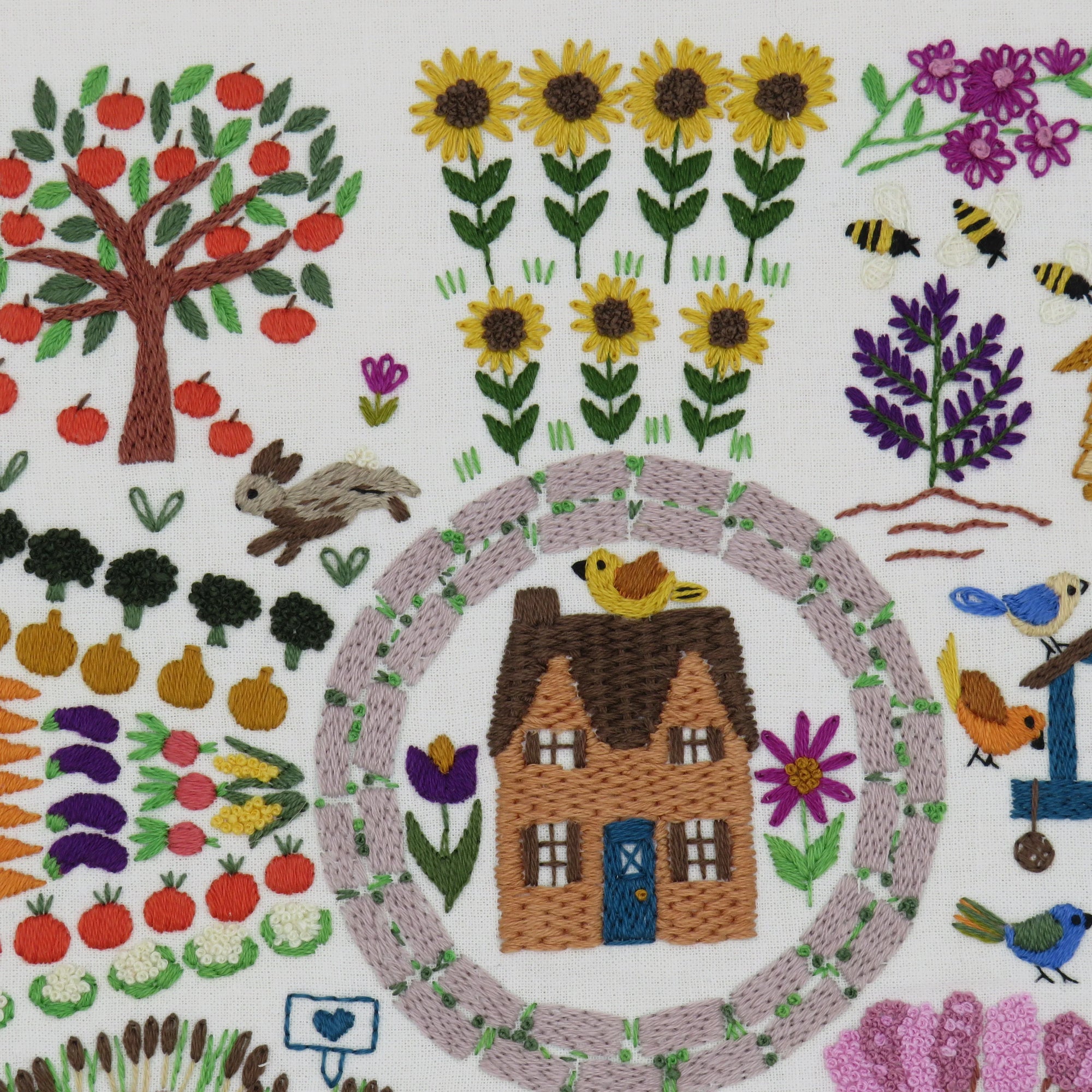 Embroidered scene with a house, garden, and animals on a white background