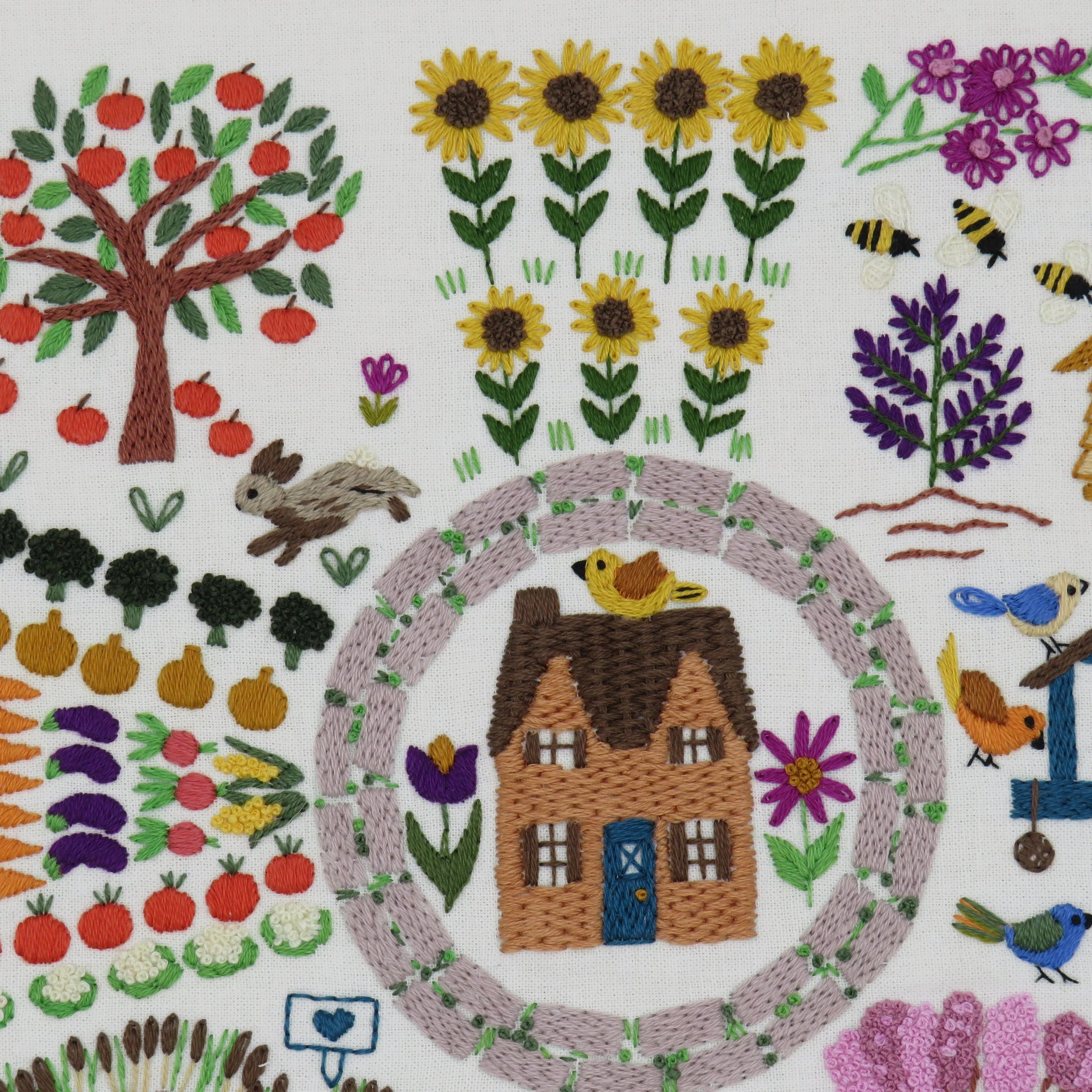 Embroidered scene with a house, garden, and animals on a white background