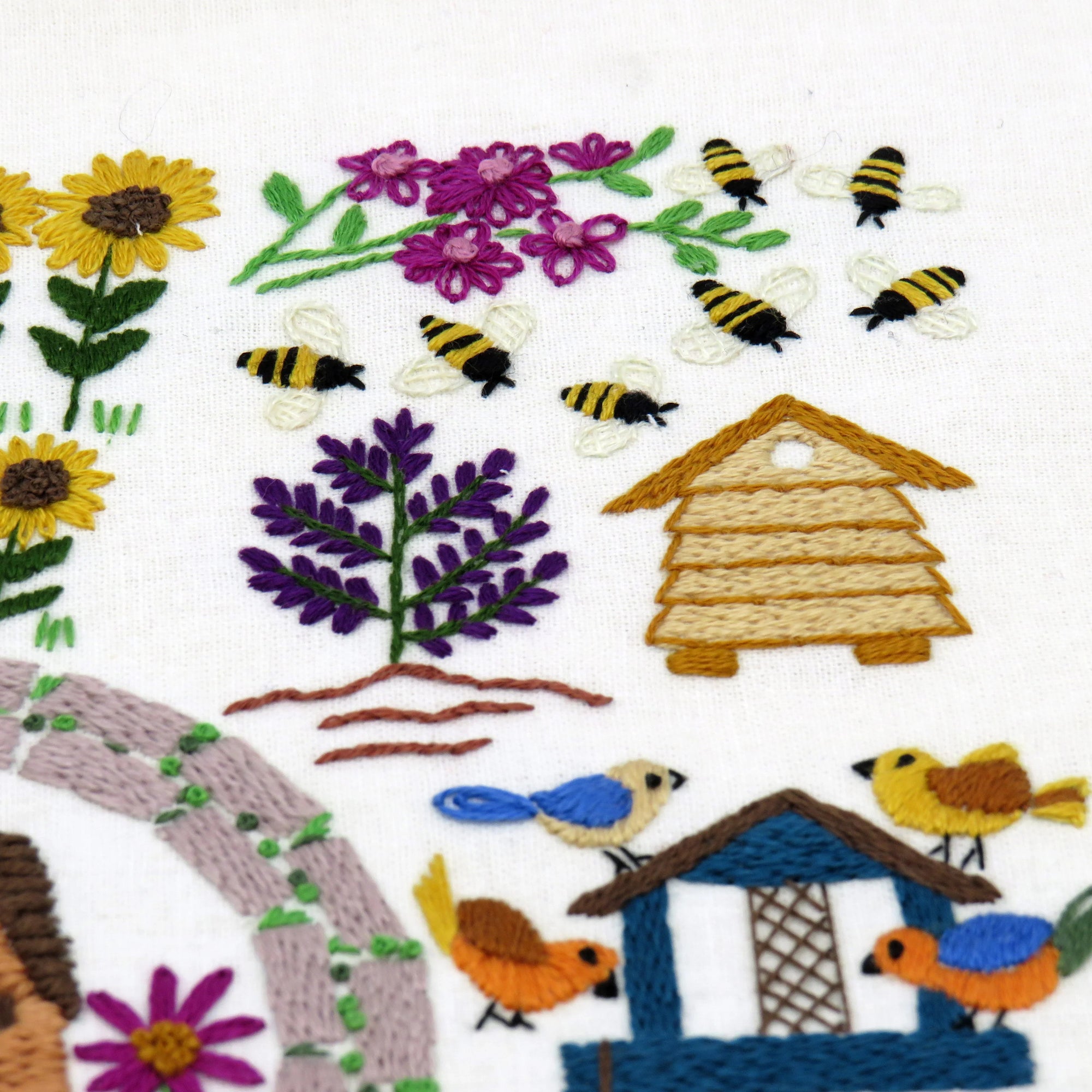 Embroidered design of bees, flowers, a beehive, and birds on a white background