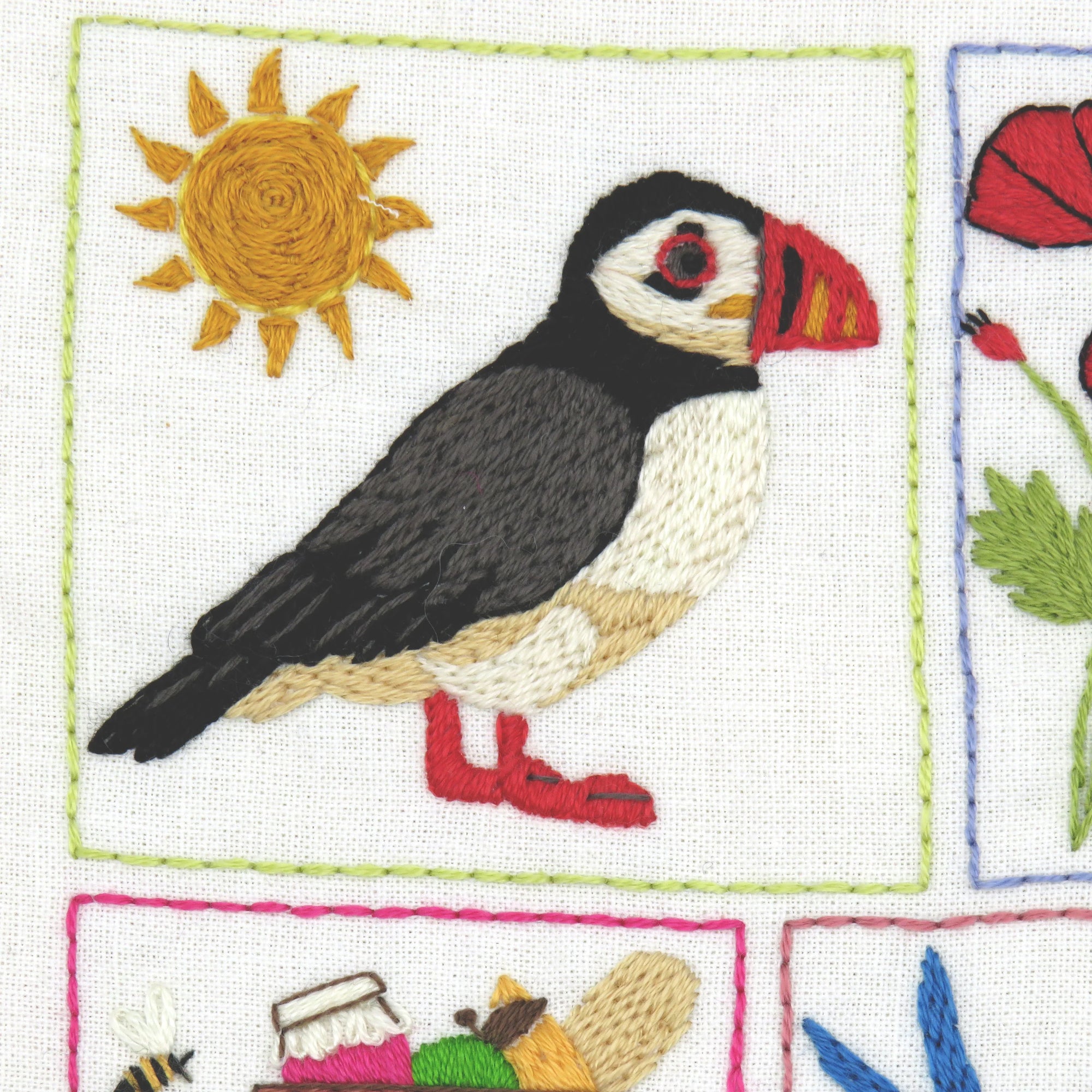 Embroidered design of a puffin with a sun and other elements on a white background