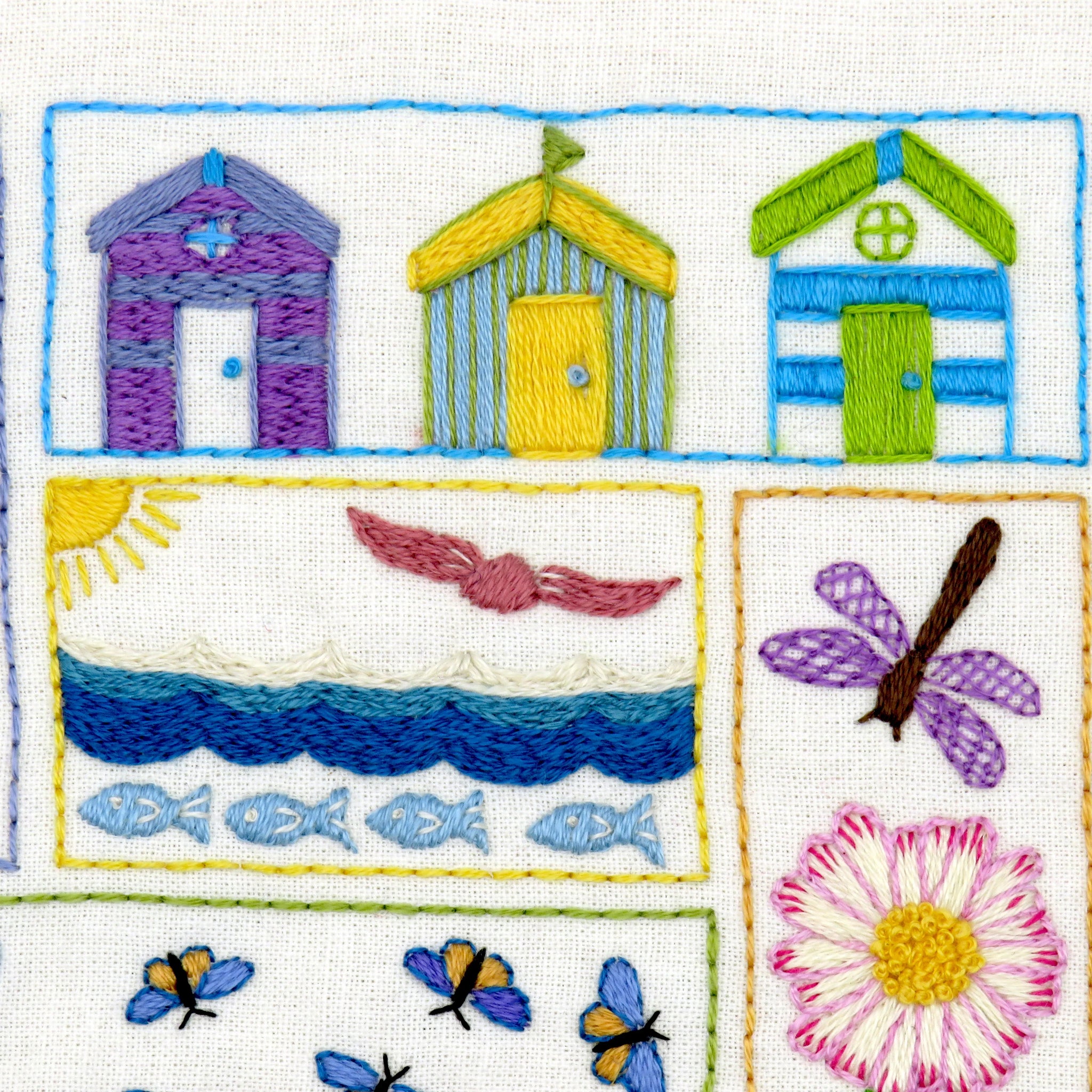 Embroidered design with beach huts, sun, dragonfly, and flowers on a white background