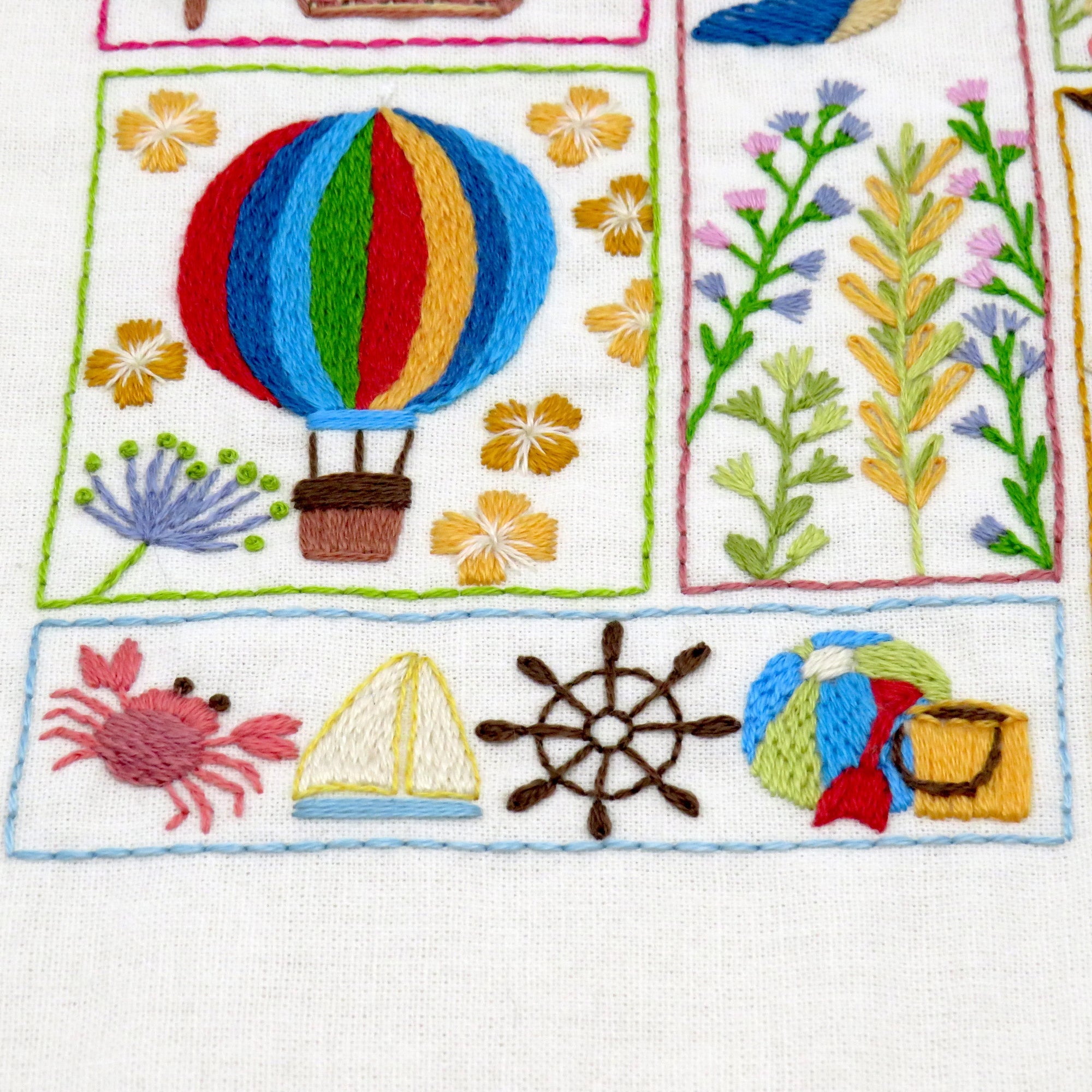 Embroidered patch with colorful hot air balloon, flowers, crab, sailboat, and wheel on a white background.