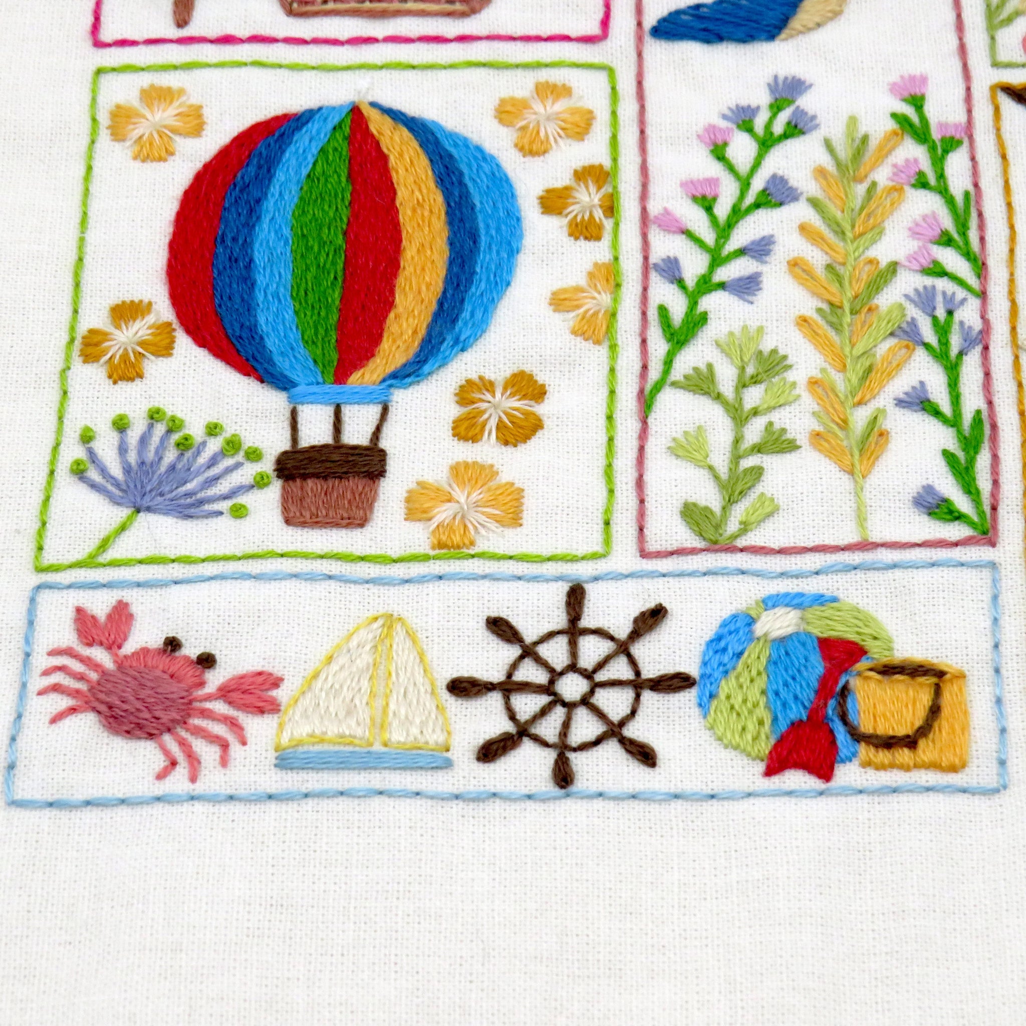 Embroidered patch with colorful hot air balloon, flowers, crab, sailboat, and wheel on a white background.