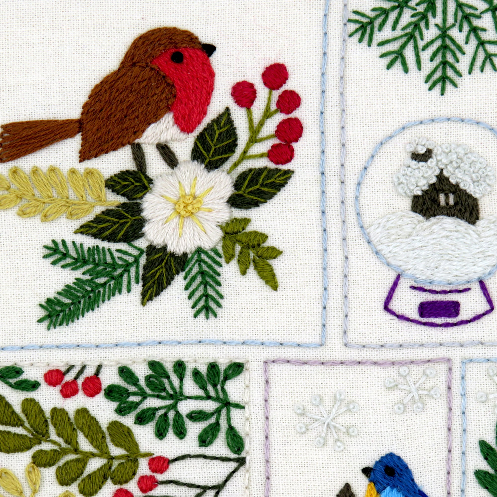 Embroidered design with a robin, snow globe, and floral elements on a white background.